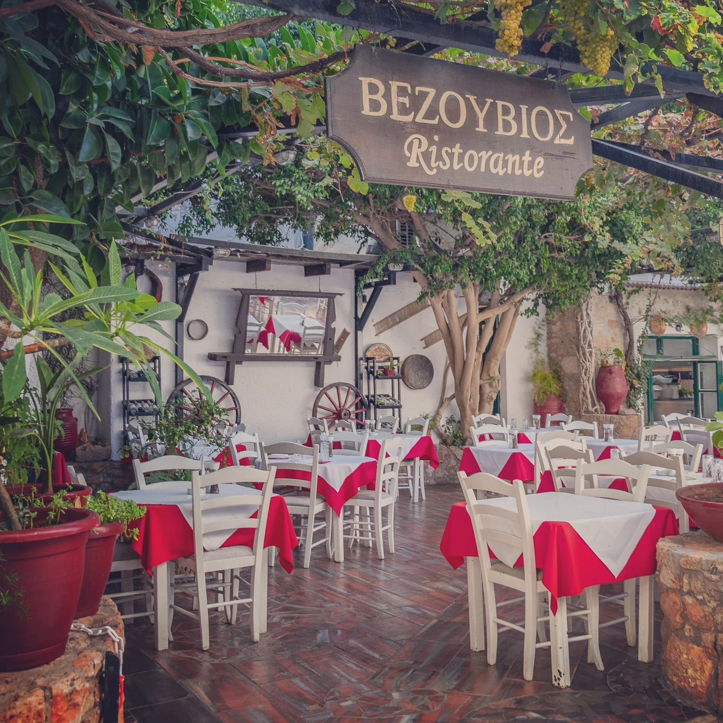 Outdoor seating area of Vezouviοs Ristorante in Hersonissos with white tables and red tablecloths.