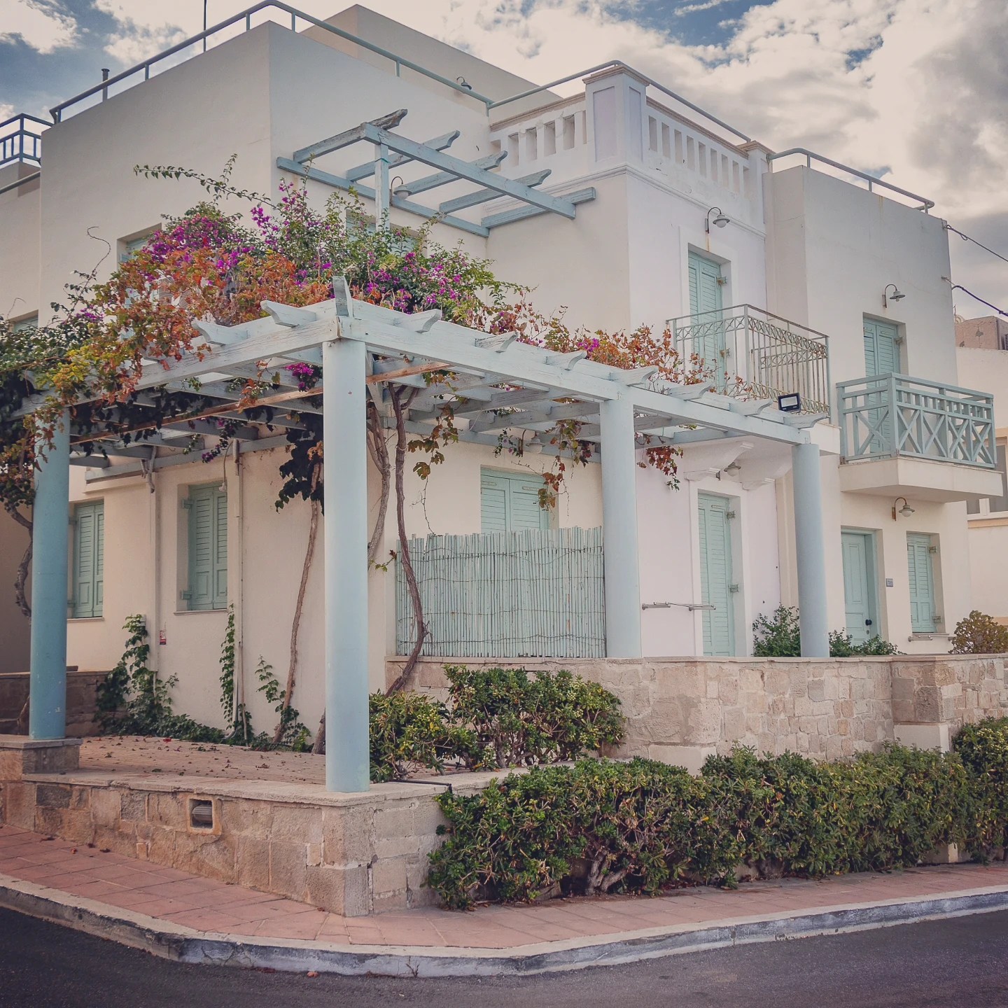 Whitewashed house with blue shutters and a pergola covered in flowering vines in Hersonissos, Crete.