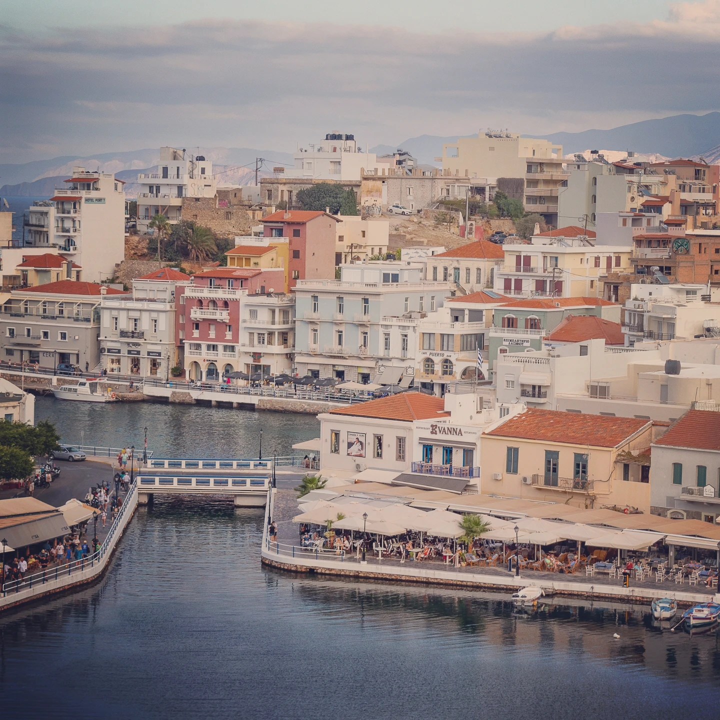 A closer elevated view of colorful buildings along the Agios Nikolaos waterfront beside the narrow channel.