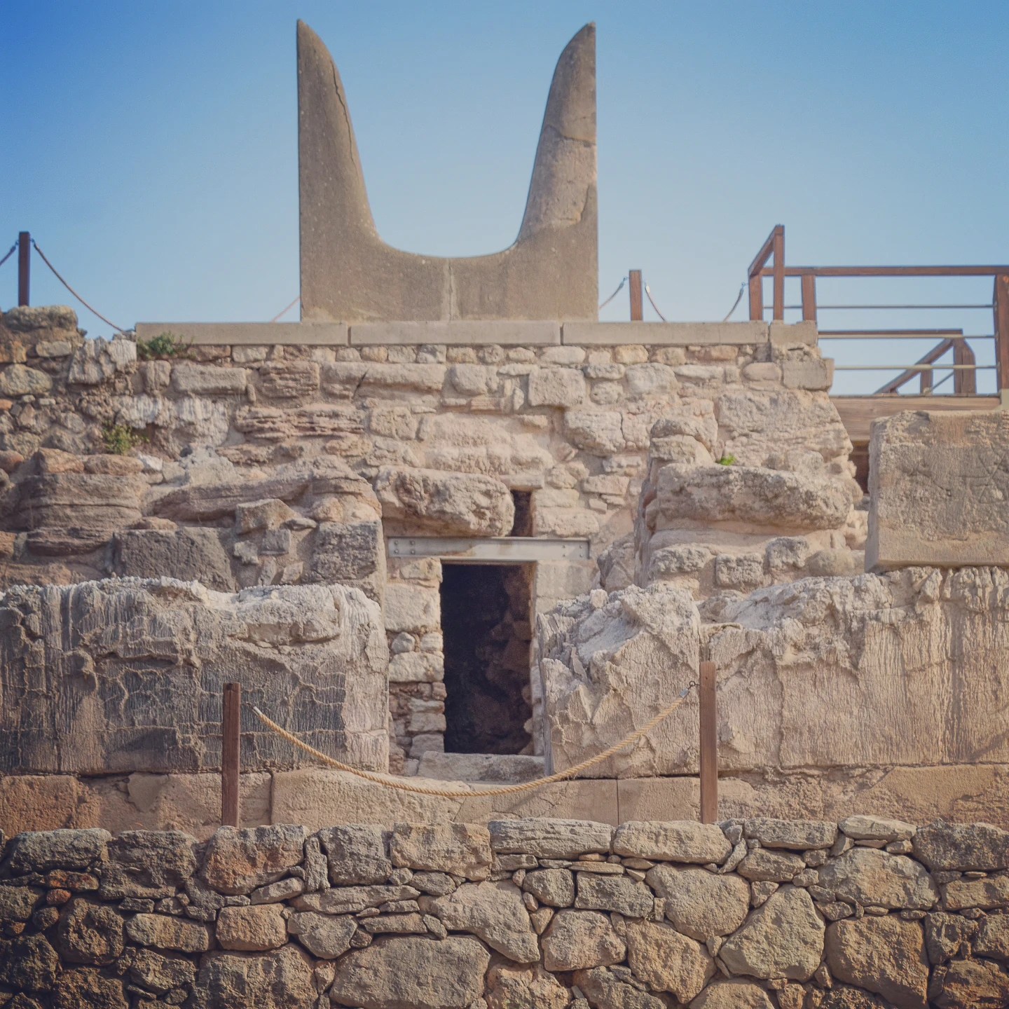 Stone ruins at Knossos topped with the famous Minoan “Horns of Consecration” against a blue sky.
