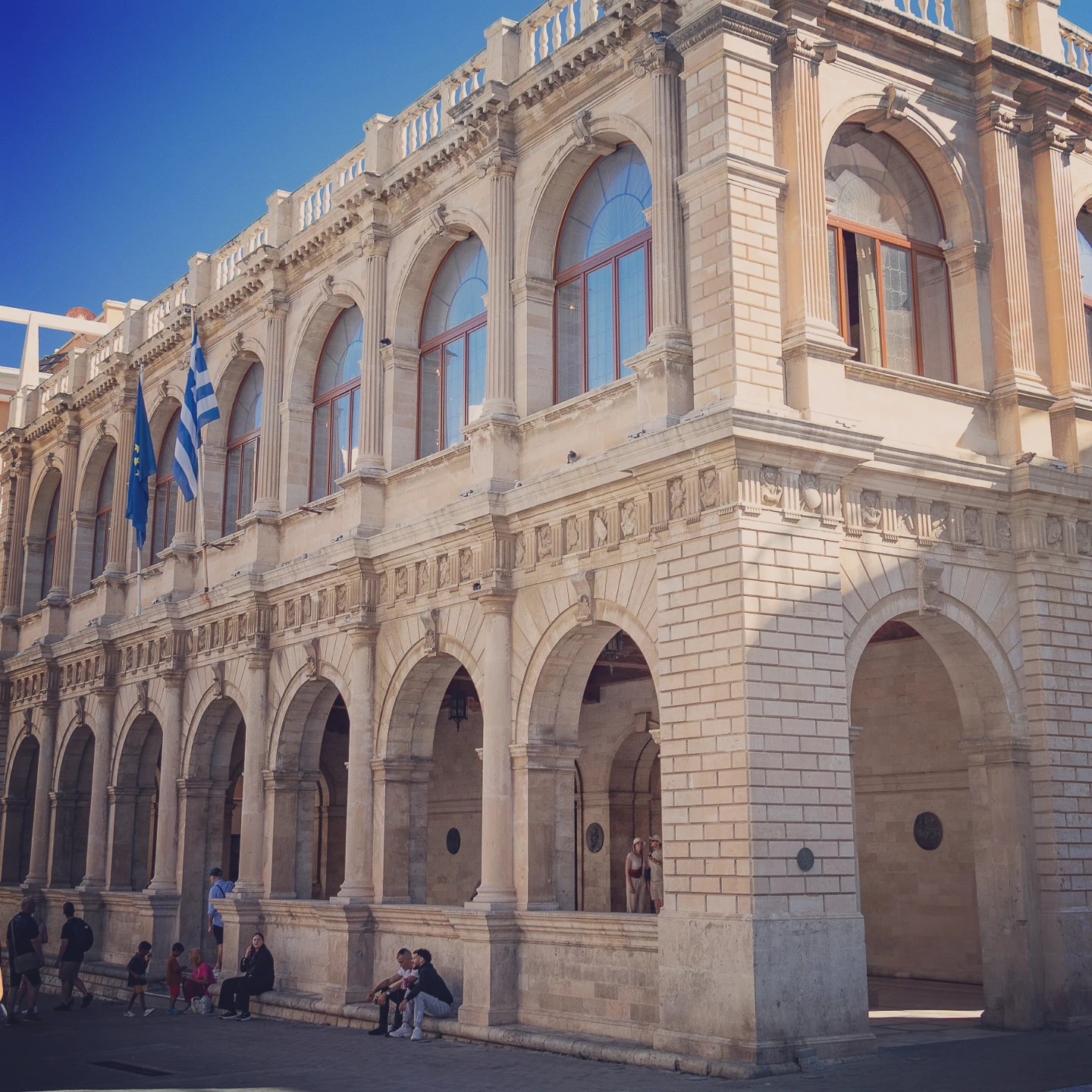 The Venetian Loggia building in Heraklion with its arches, columns, and flags displayed on the façade.