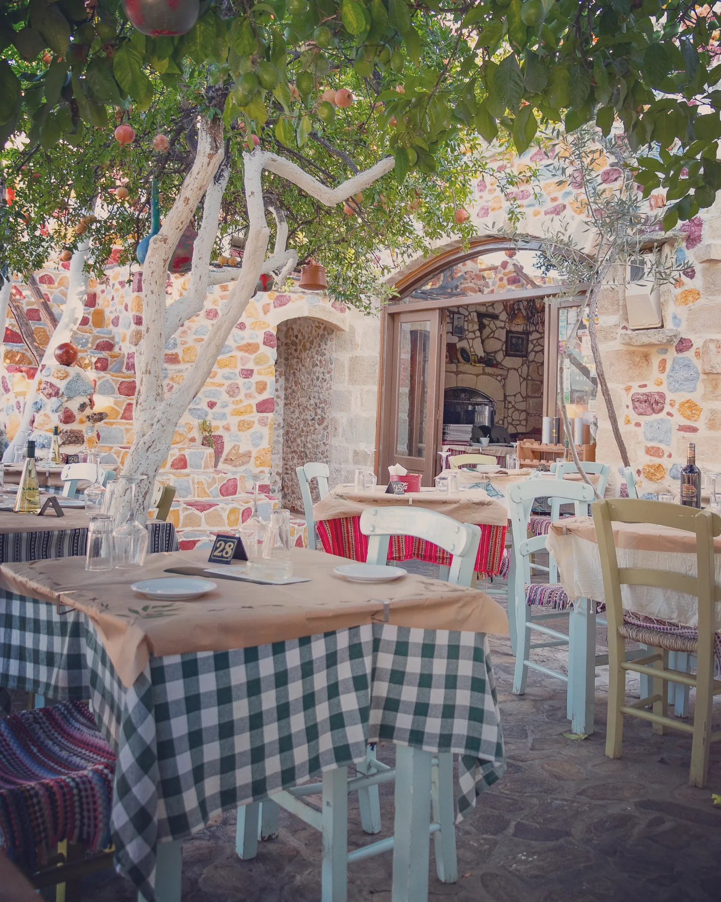Traditional outdoor taverna in Ano Hersonissos with stone walls, pomegranate trees, and checkered tablecloths.