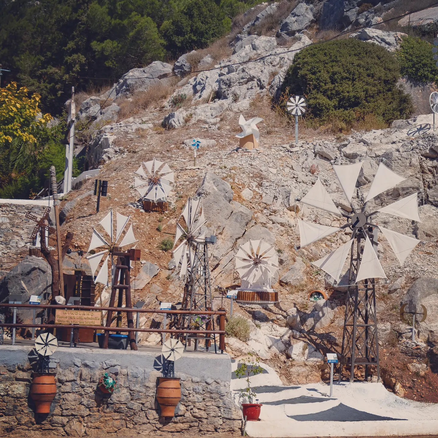 Outdoor display of small decorative windmill models arranged on a rocky hillside near the Lasithi Plateau.