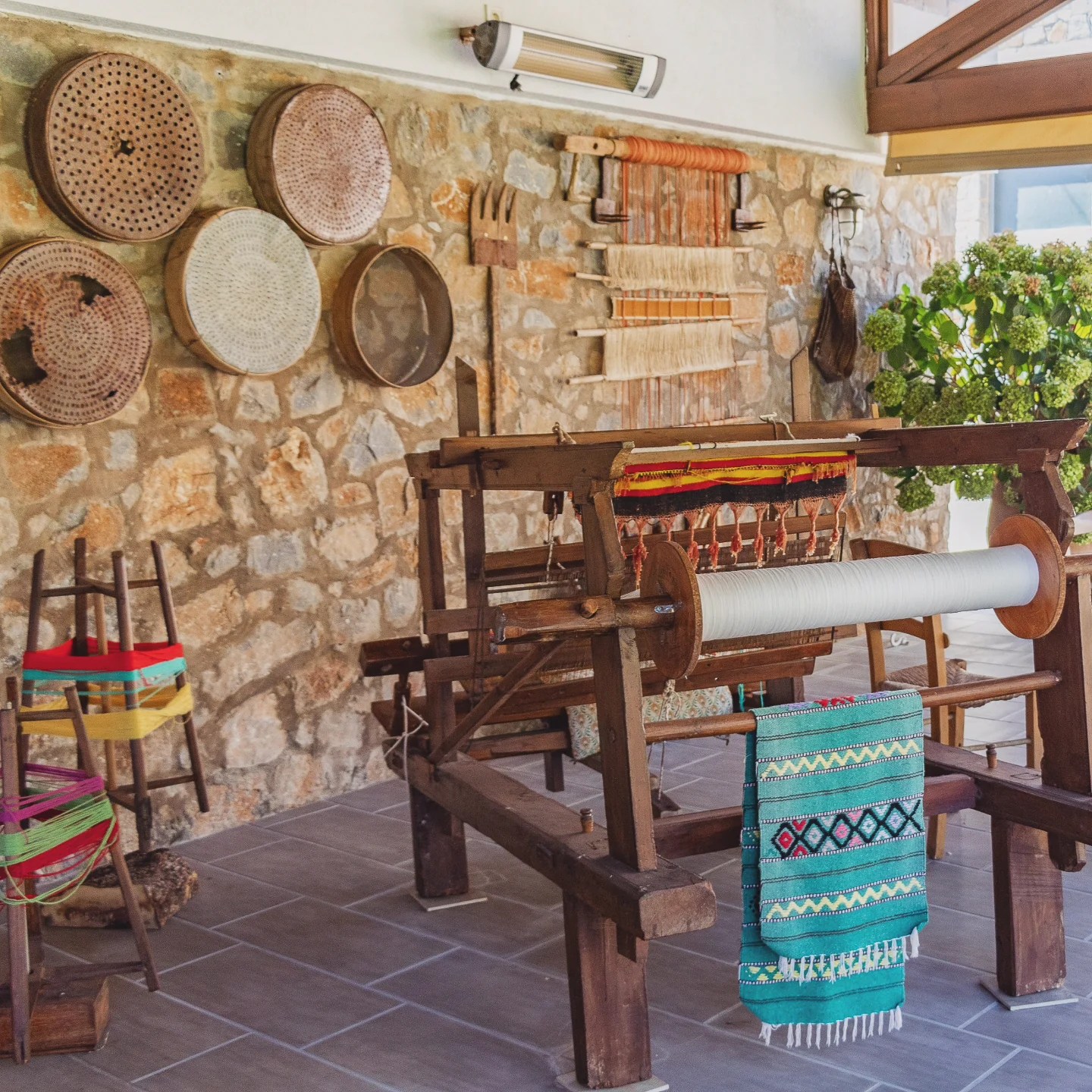 Traditional wooden loom with colorful woven fabric and old tools displayed against a stone wall.