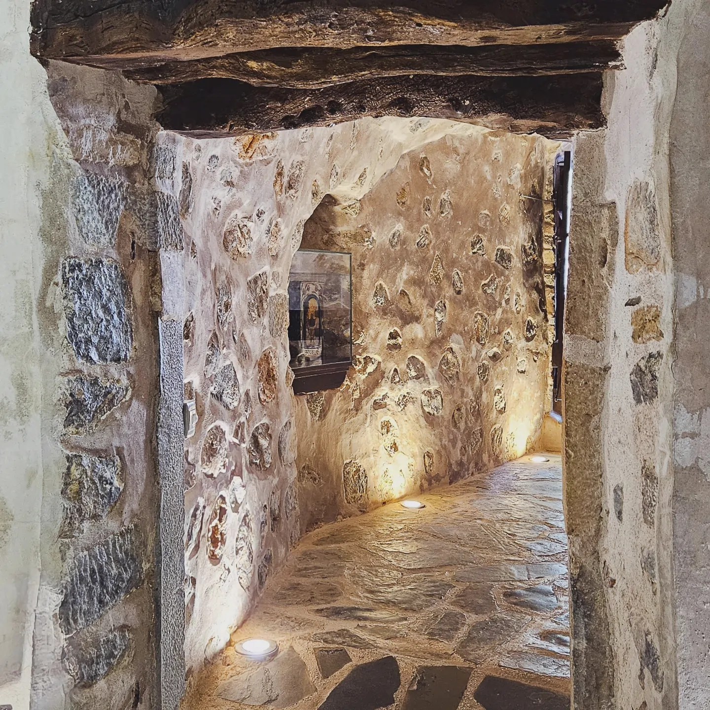 Curved stone passageway inside the Monastery of the Panayia Kera with warm lighting and exposed wooden beams.