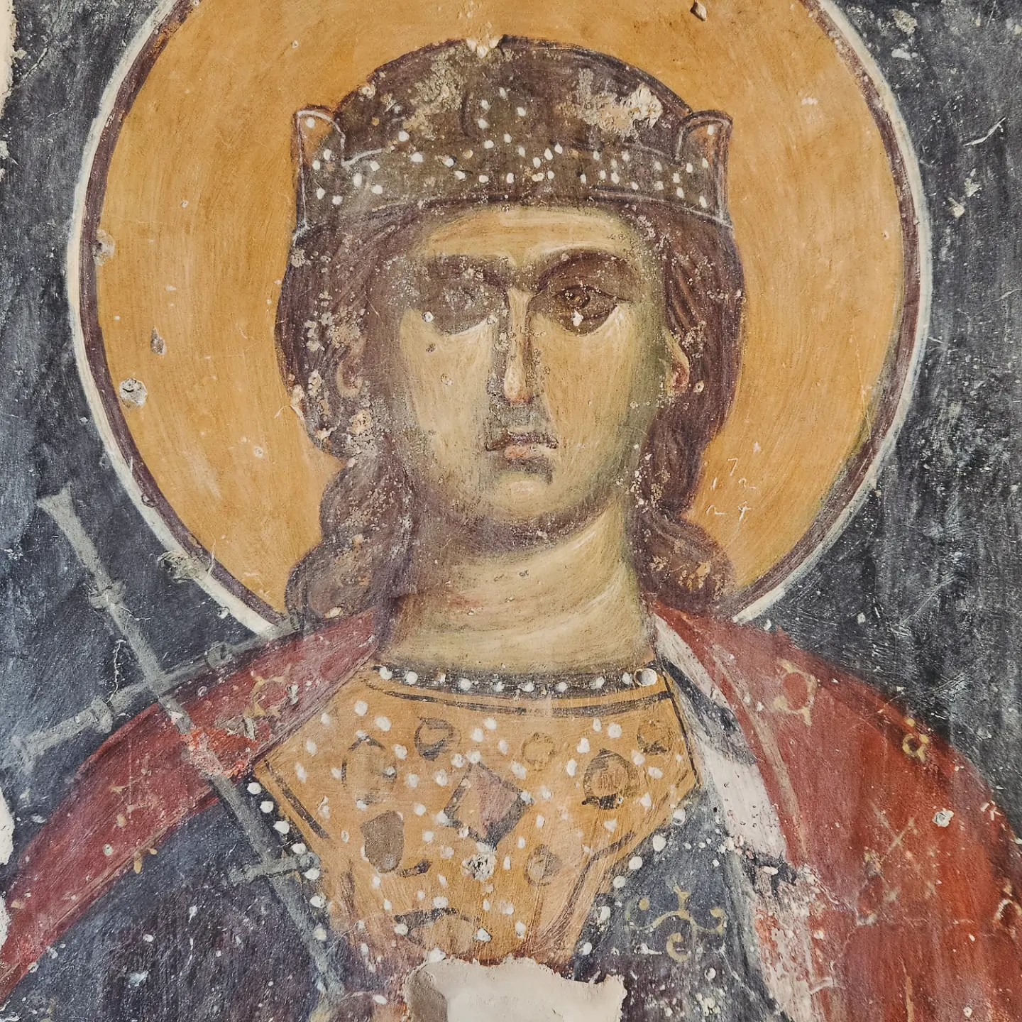Close-up of a Byzantine fresco showing a saint with a golden halo, jeweled crown, and patterned robes.
