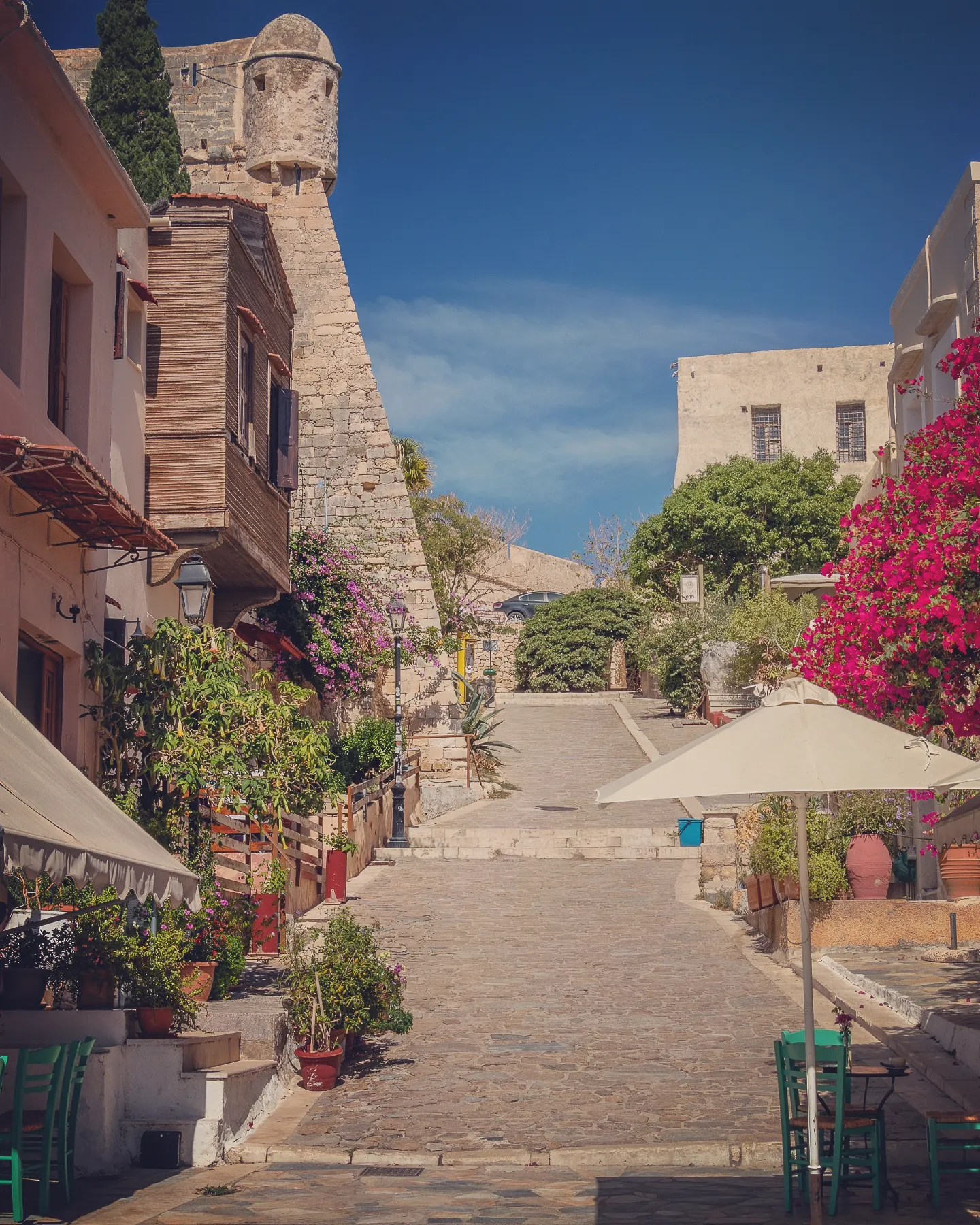 A sloped stone street in Rethymno lined with flowers and houses, leading up to part of the Fortezza’s walls.