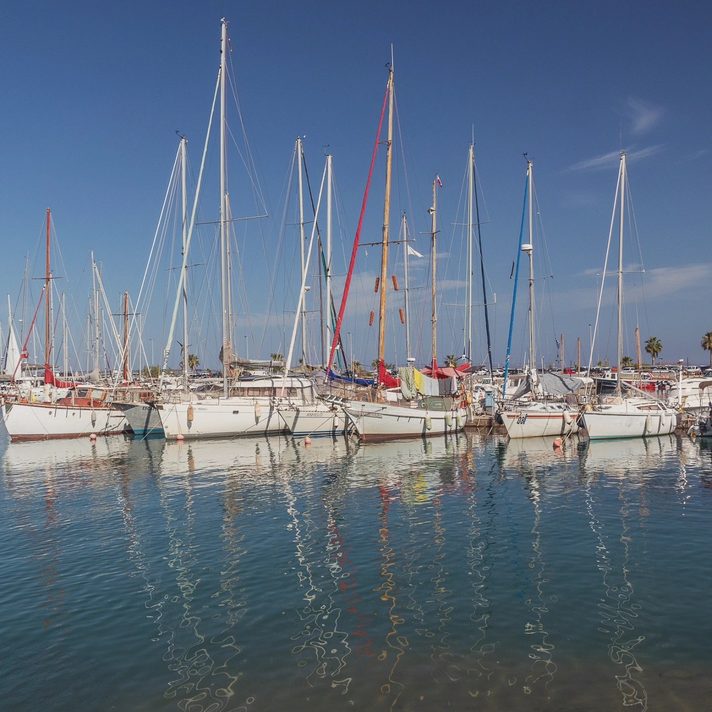 A row of sailboats lined up in Rethymno’s marina with their masts reflected in the calm water.