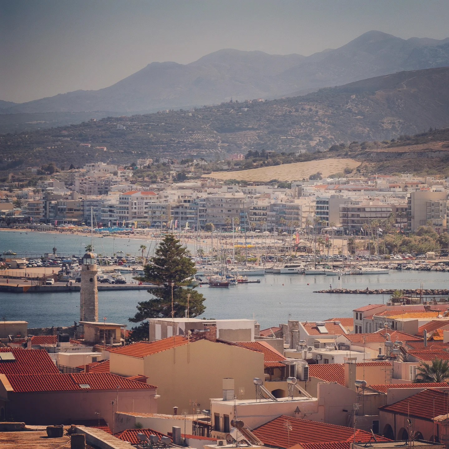 A view of Rethymno with red rooftops, the marina full of boats, and mountains rising in the background.