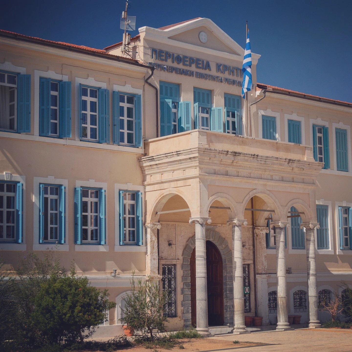 The cream-colored Rethymno Regional Unit building with blue shutters and an arched portico.