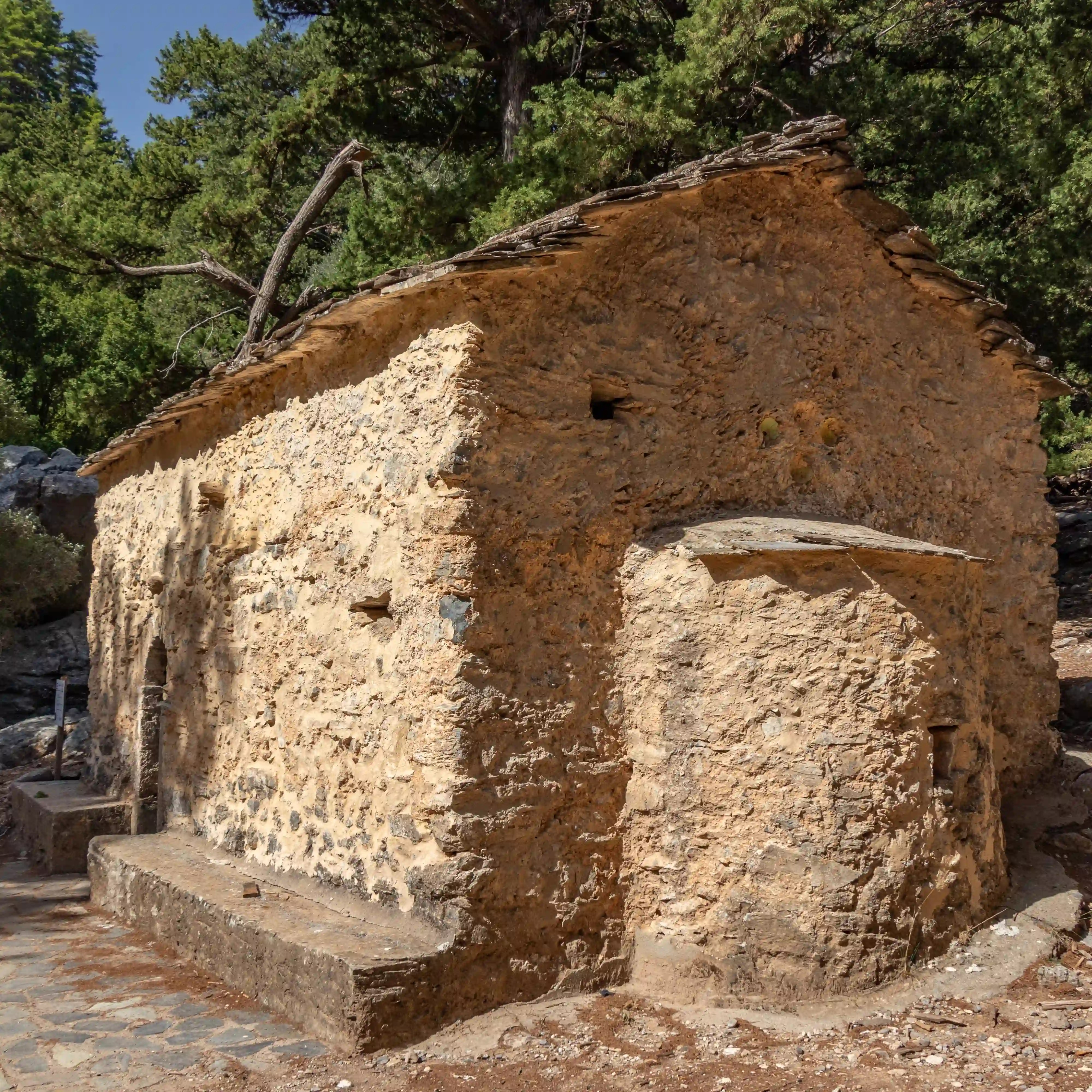 Old stone chapel with a simple roof surrounded by pine trees in the Samaria Gorge.