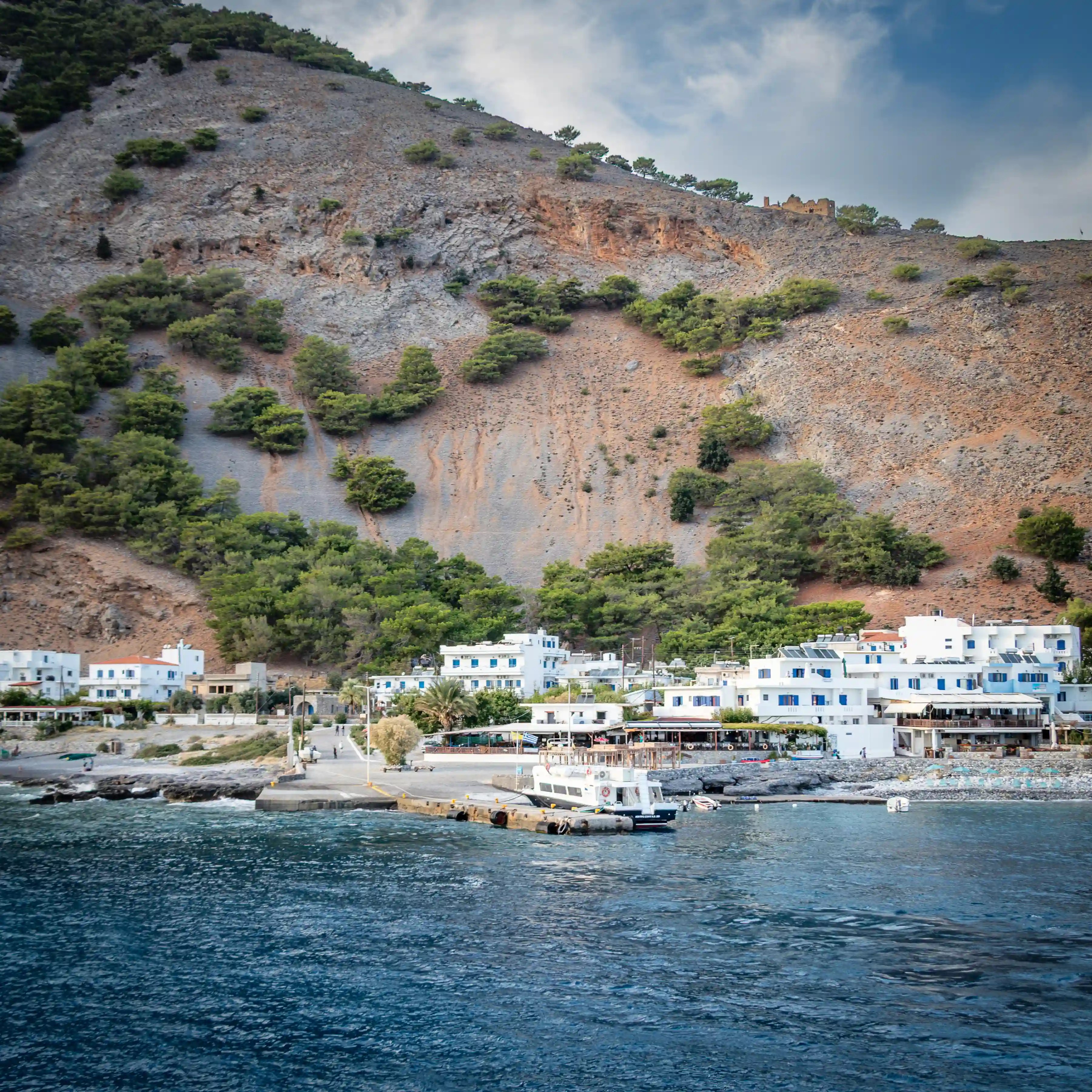 White buildings of Agia Roumeli at the base of a steep rocky mountain beside the sea.