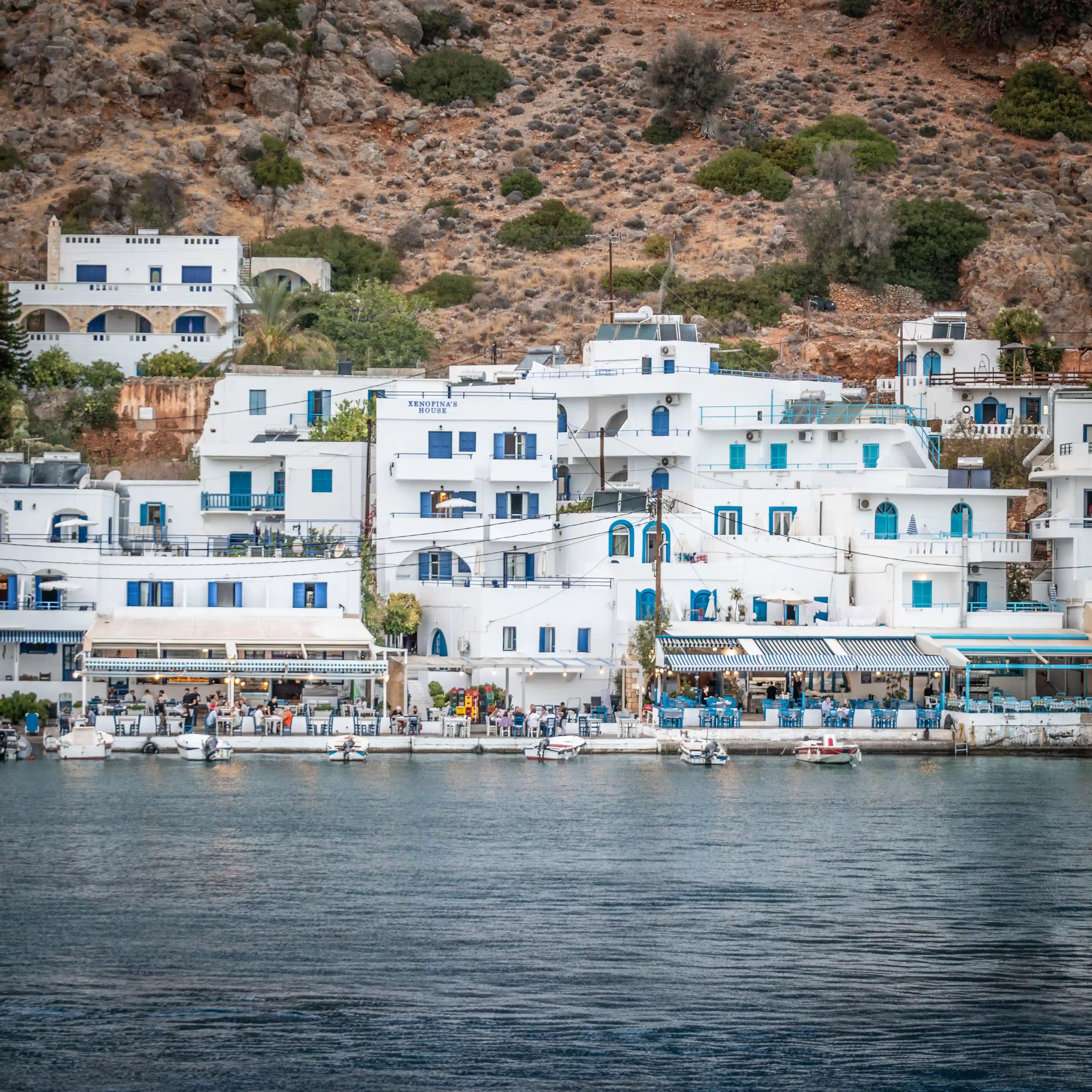 White hillside buildings with blue accents overlooking the water and rocky terrain.