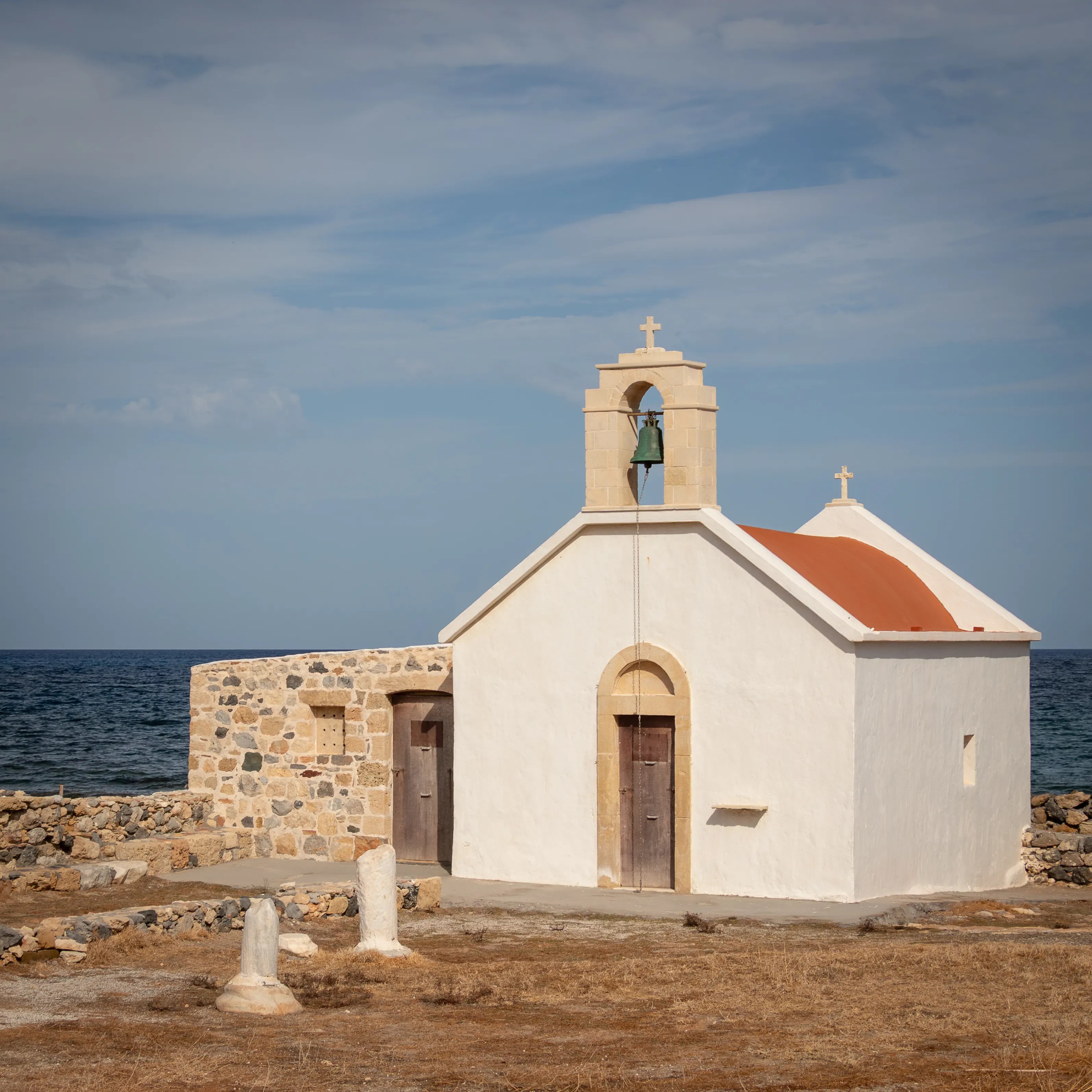 Small white chapel with a terracotta roof and bell tower near the shoreline in Hersonissos.