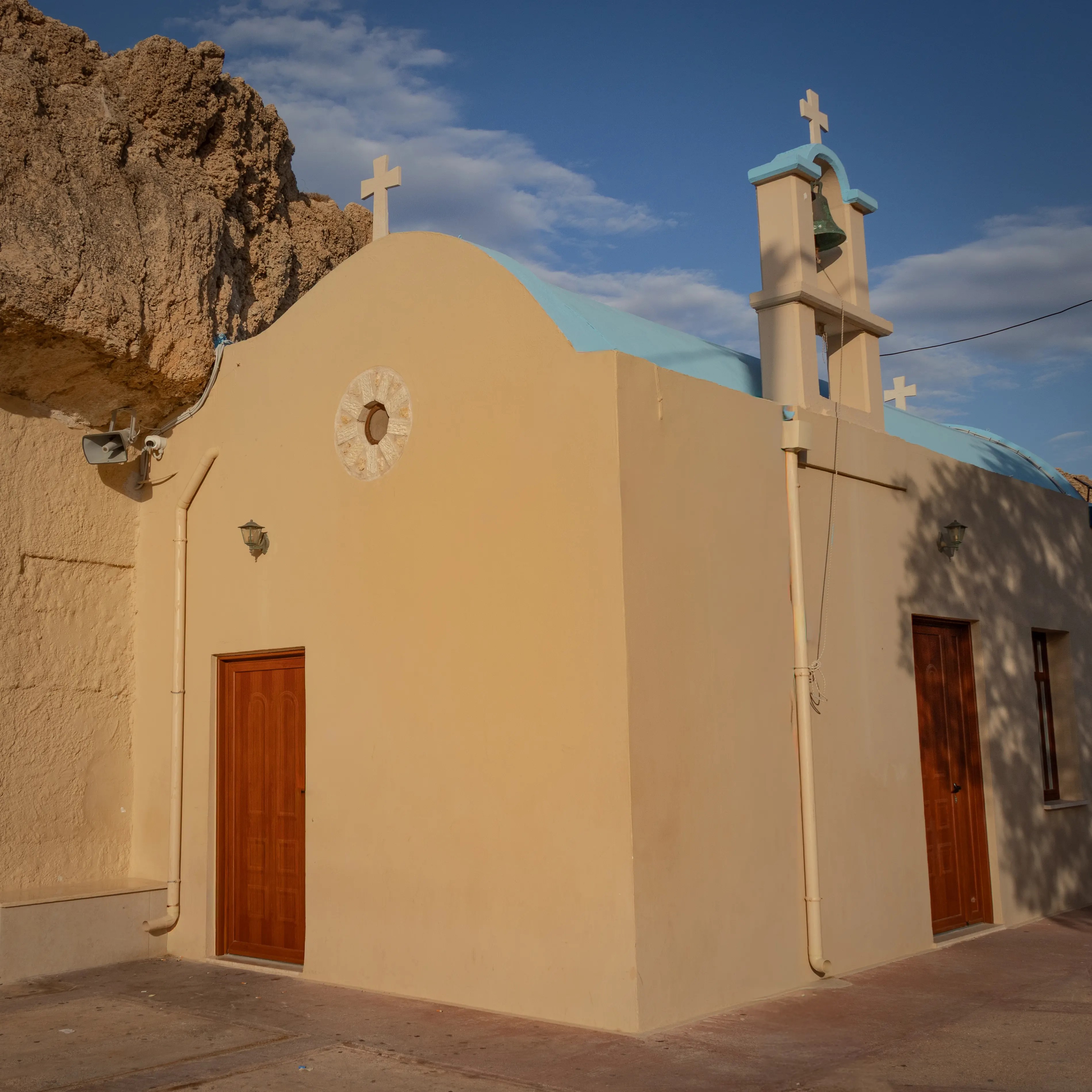 Church of Saint Paraskevi in Hersonissos, a small beige seaside chapel with a blue-topped bell tower and crosses.