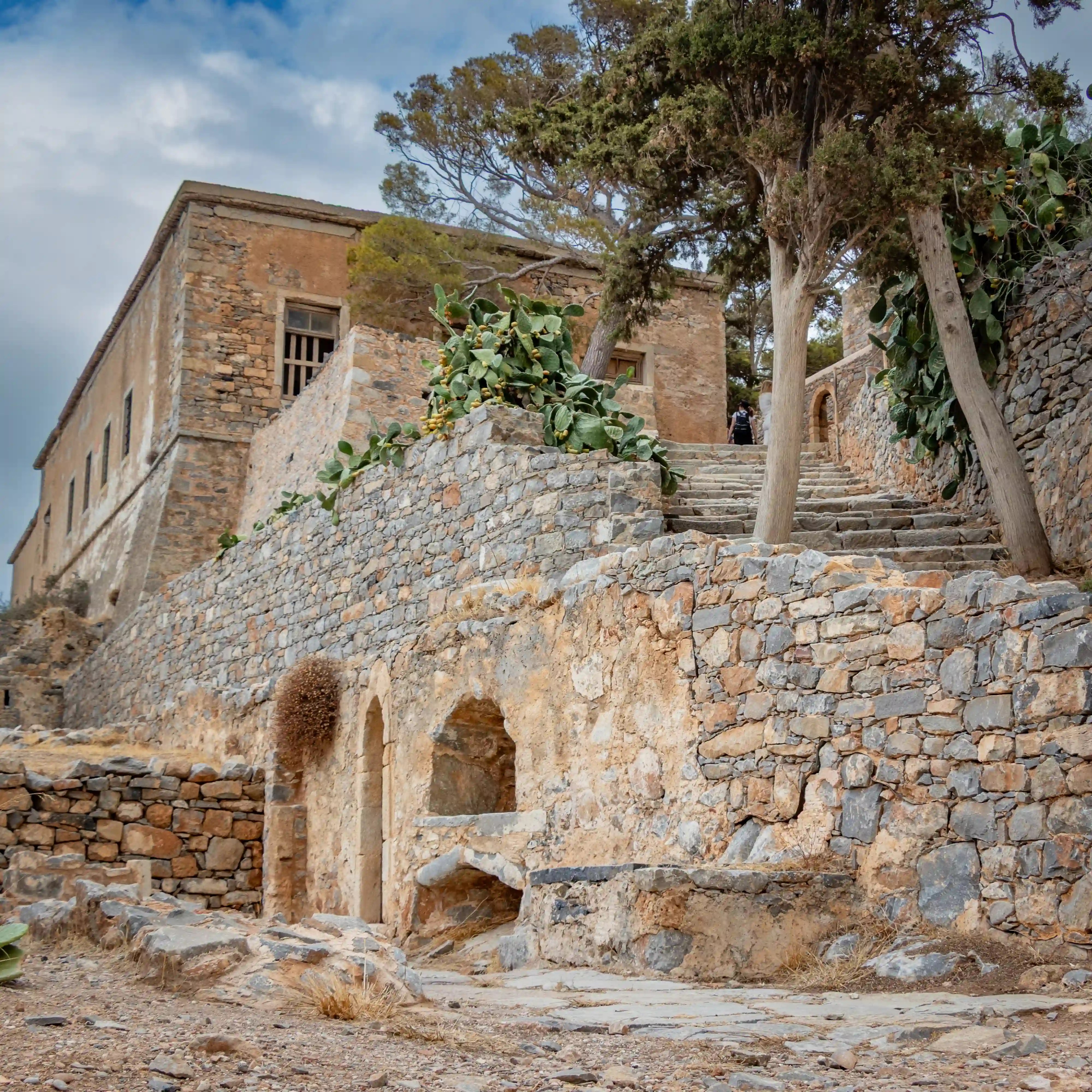 A stone stairway lined with cactus plants leads up past old buildings within Spinalonga’s fortress.
