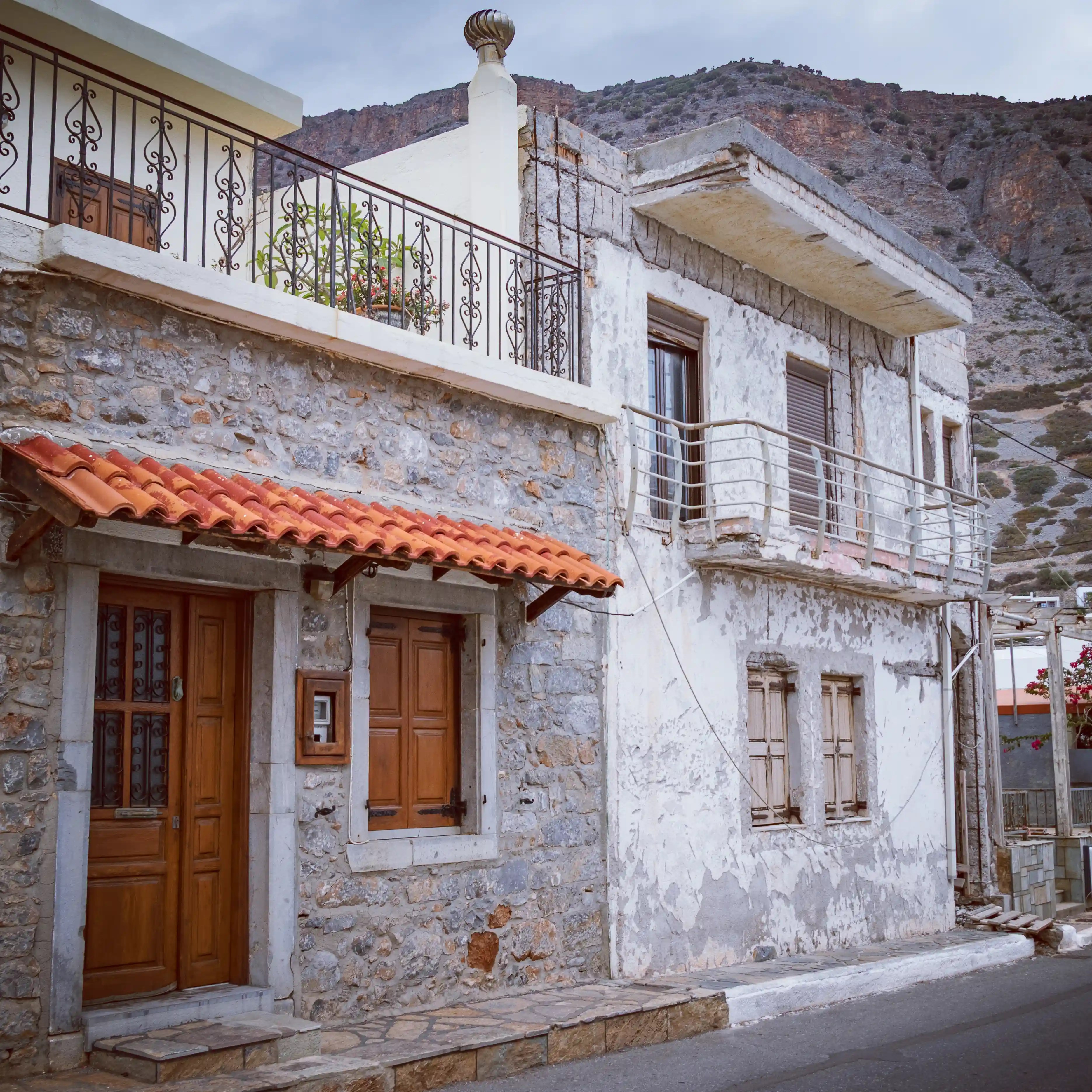 Traditional stone houses in Plaka with wooden doors and orange-tiled roofs beneath a rocky hillside.