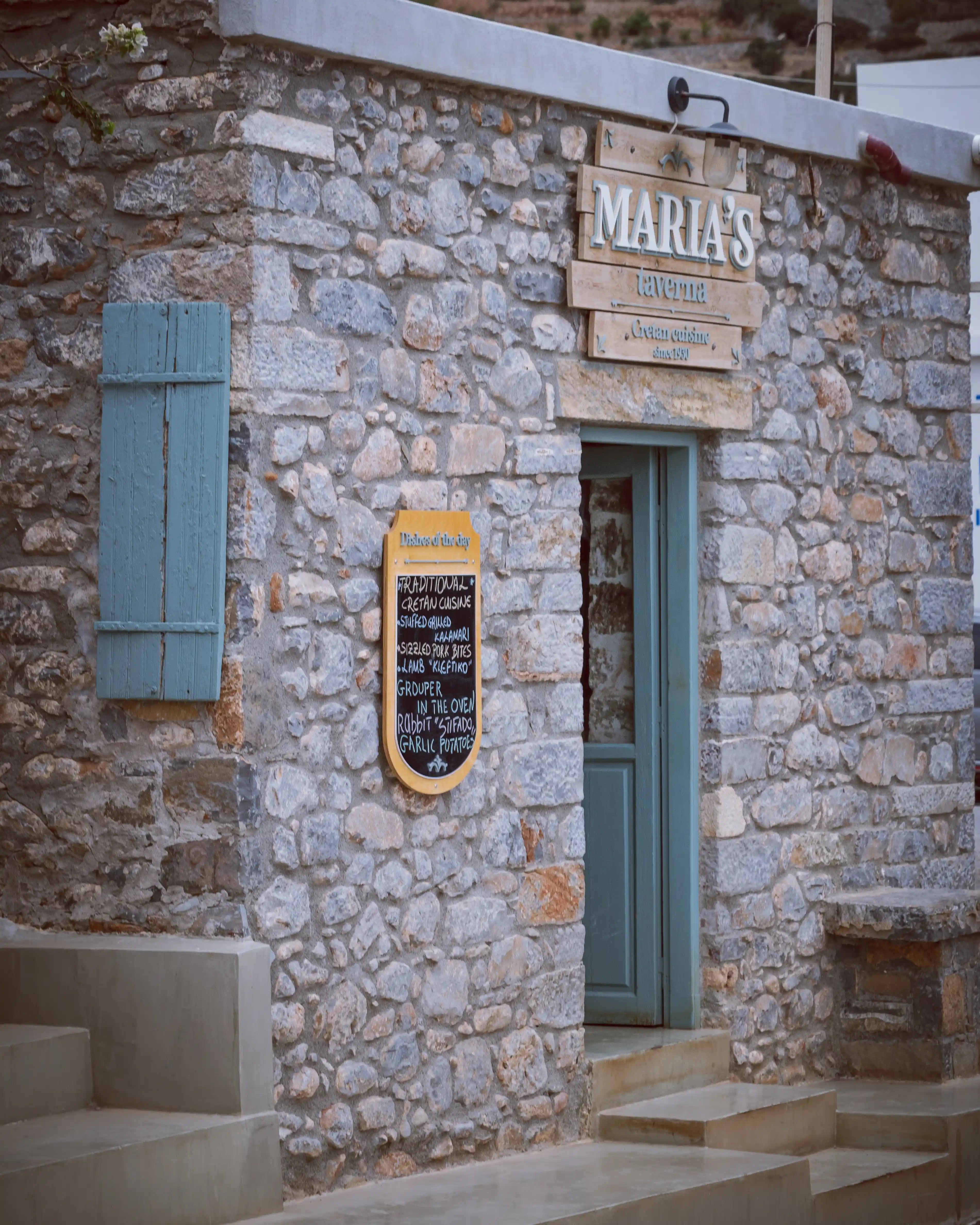 The stone exterior of Maria’s Taverna in Plaka with a blue door and chalkboard menu outside.
