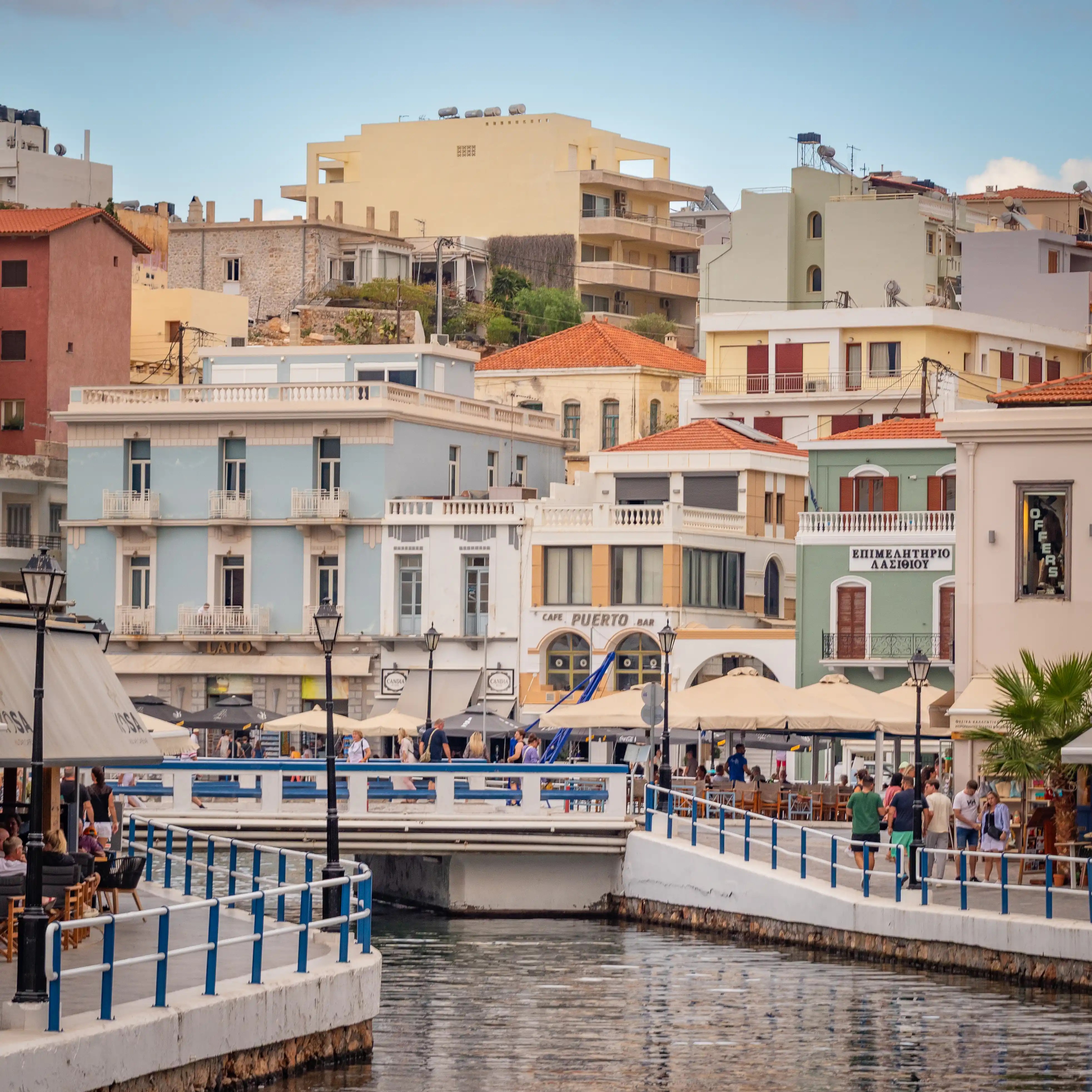Buildings and cafés surrounding the pedestrian bridge at Voulismeni Lake in Agios Nikolaos.