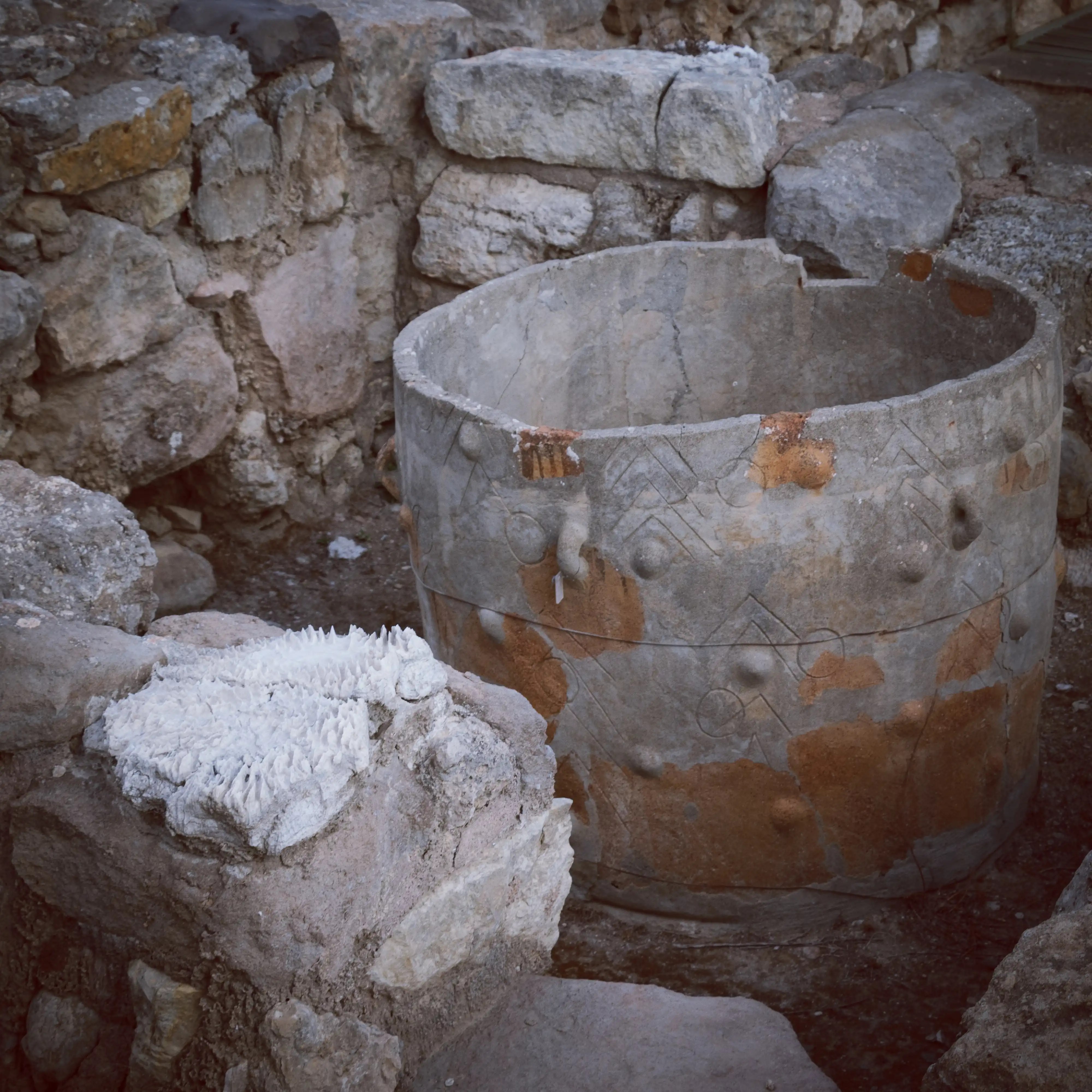 Ancient decorated stone pithos at Knossos surrounded by rubble.