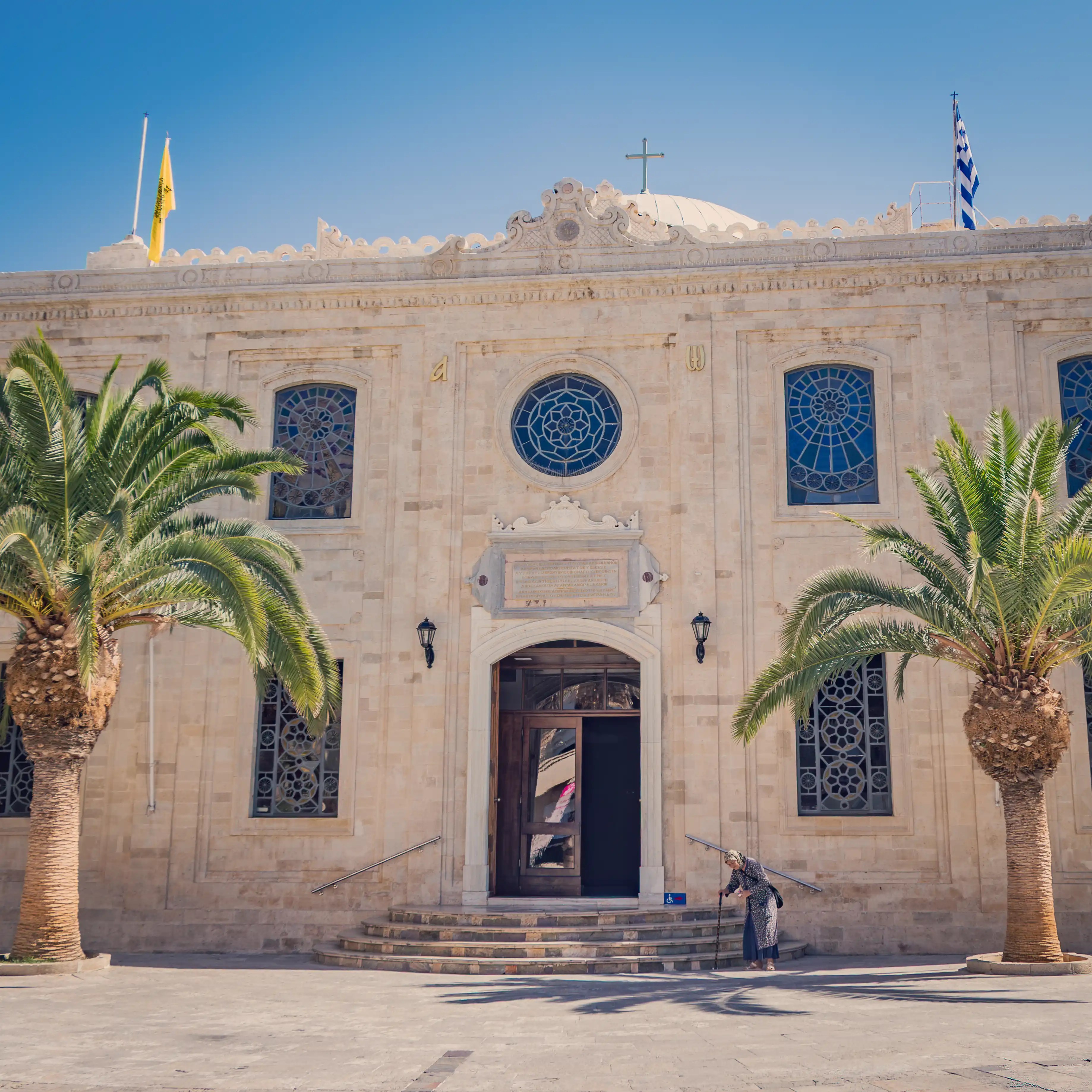 View of Agios Titos Church with large stained-glass windows and palm trees.