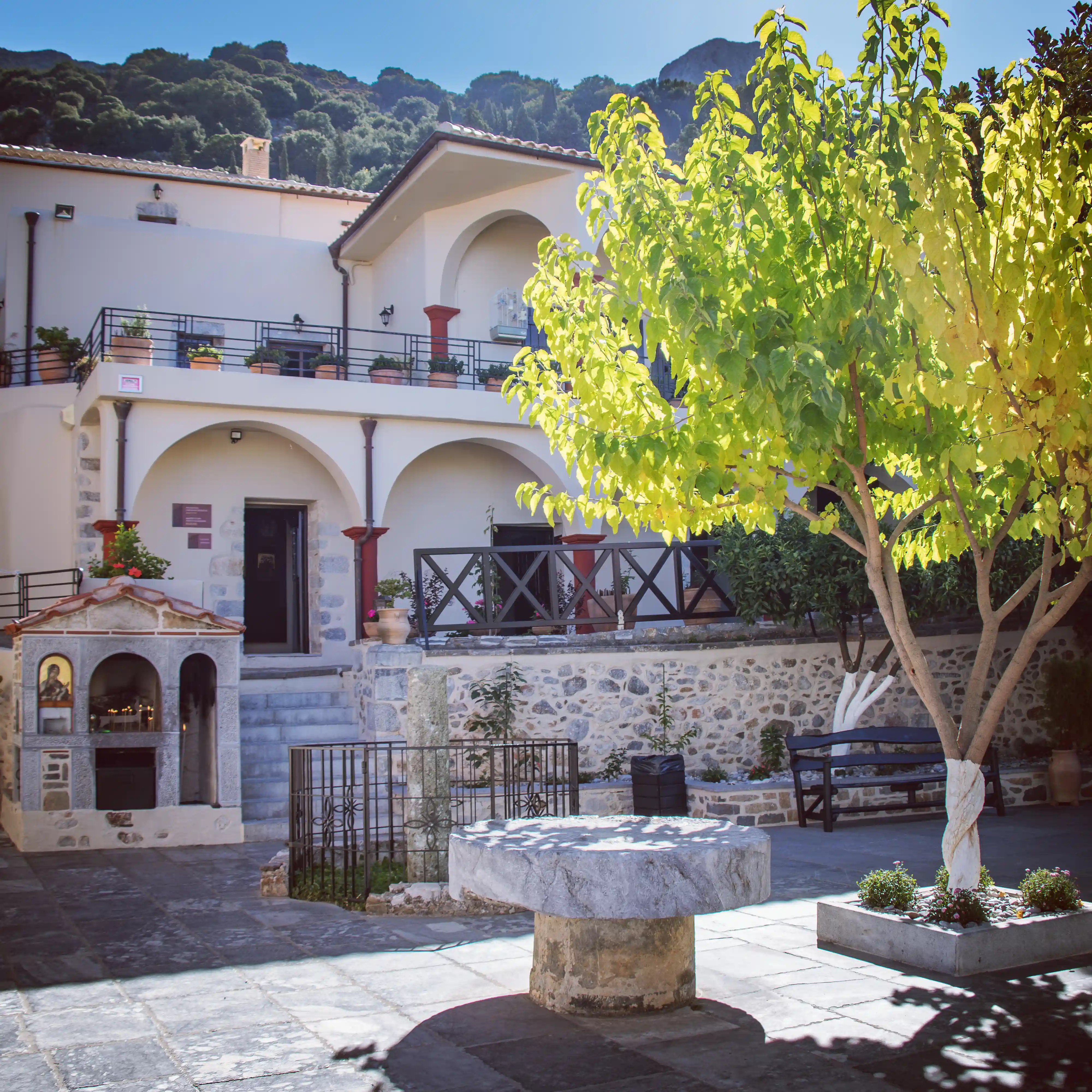 Courtyard at the Monastery of the Panayia Kera with arched walkways, stone walls, a small shrine, and a bright green tree.