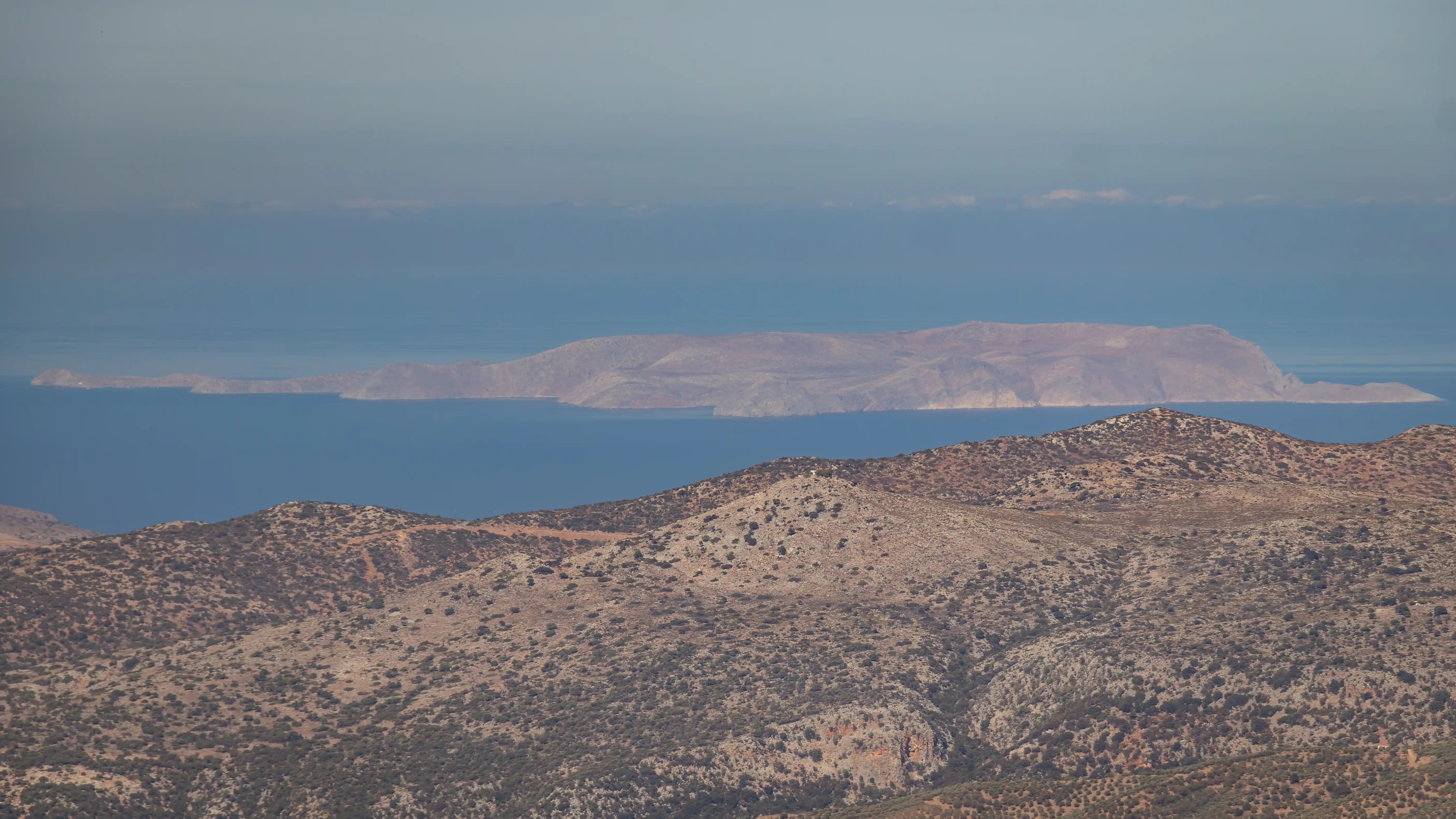 Distant offshore island seen across deep blue water and rocky hills in Crete.