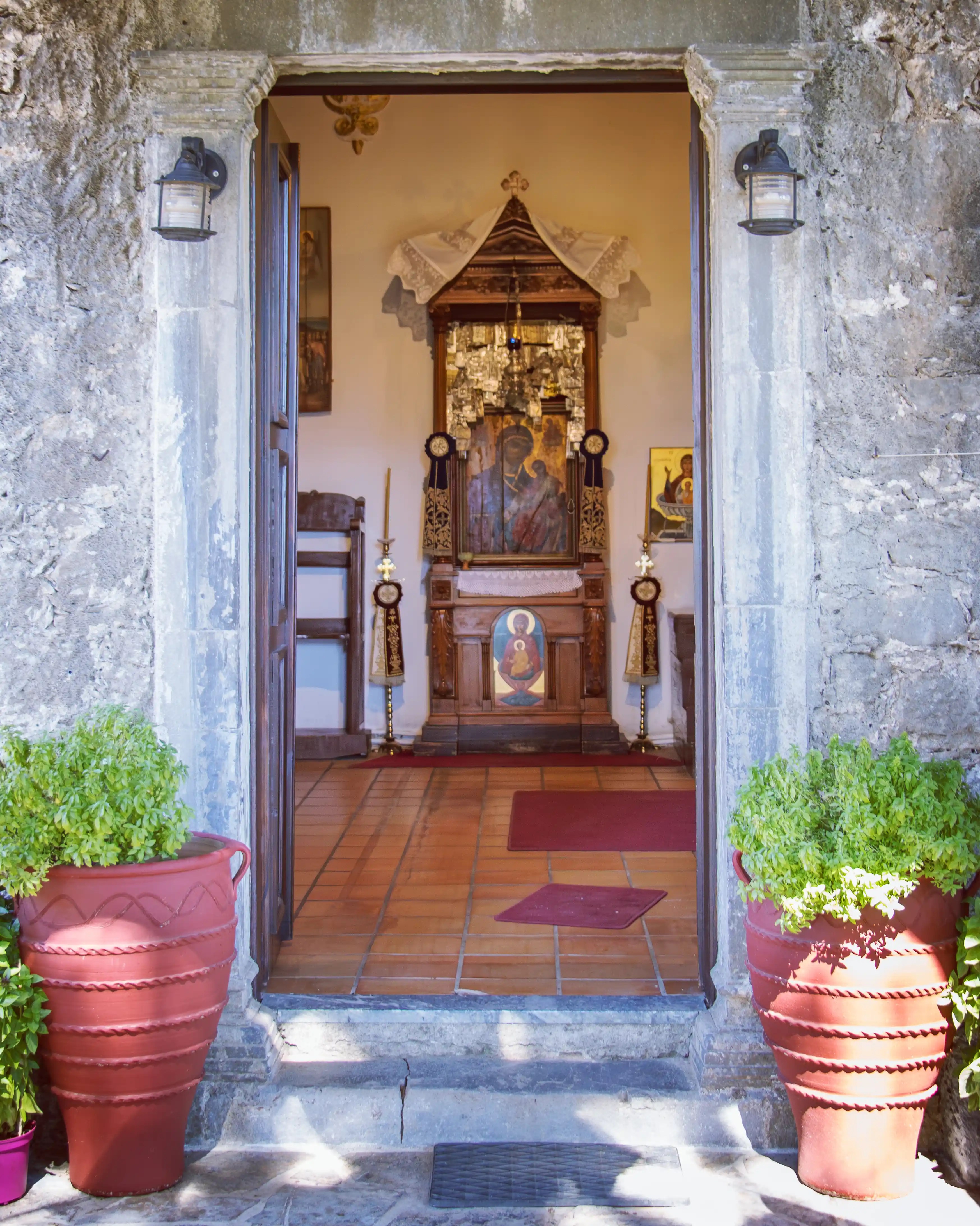 Entrance to the chapel at the Holy Monastery of Vidiani with potted plants and an icon visible inside.