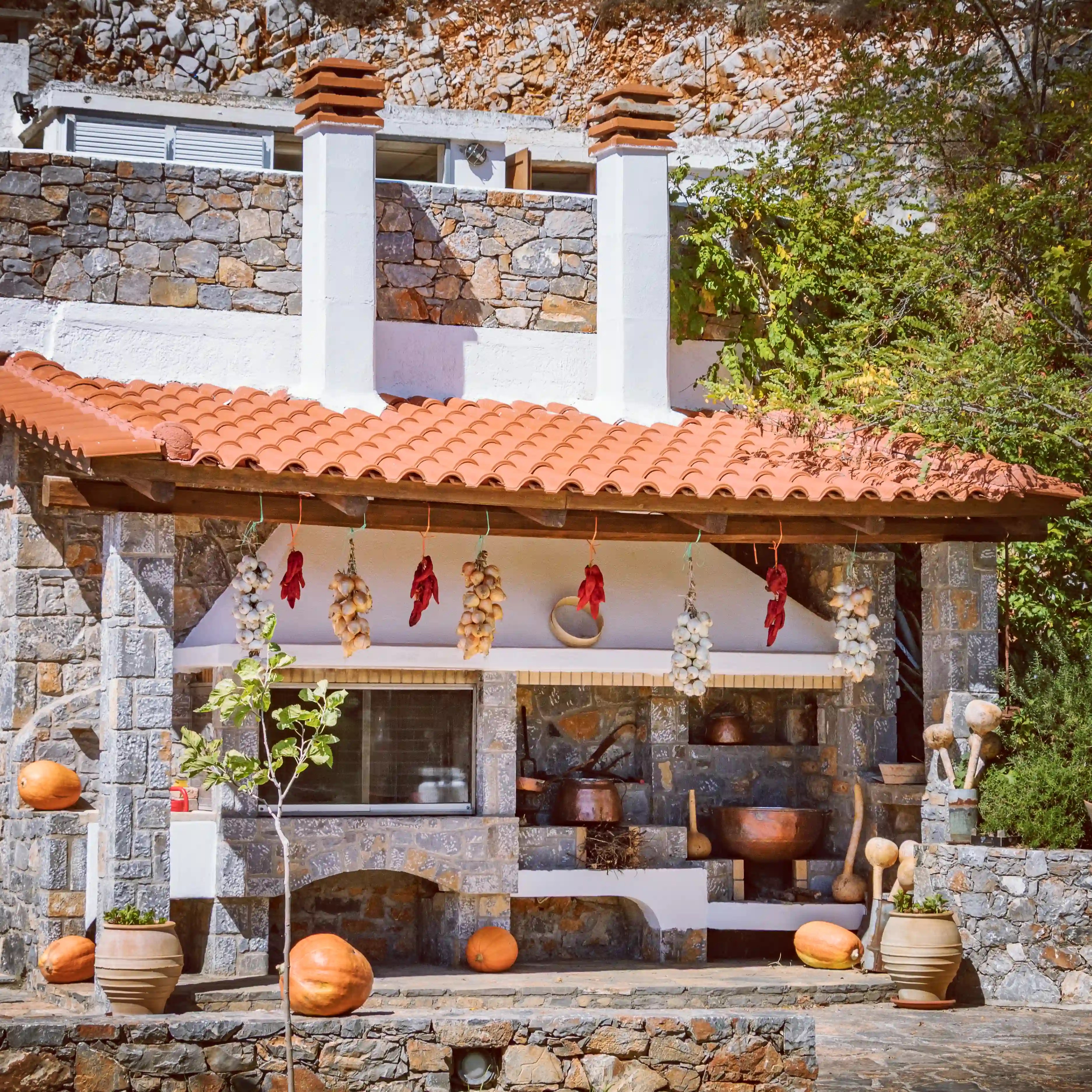 Traditional stone-and-whitewashed outdoor restaurant with hanging garlic, dried peppers, pumpkins, and copper cooking pots.