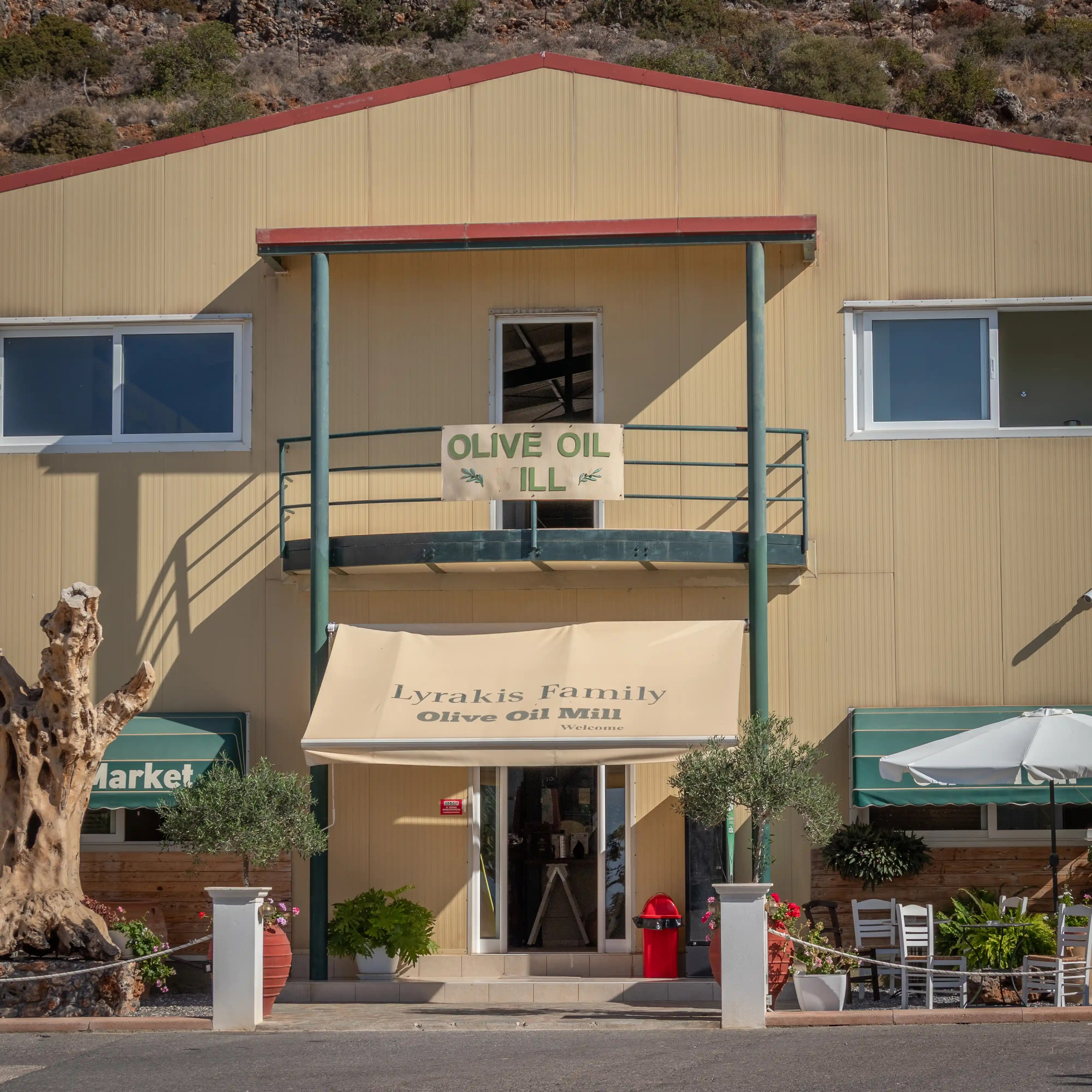 Exterior view of the Lyrakis Family Olive Mill building with awnings, potted plants, and outdoor seating.