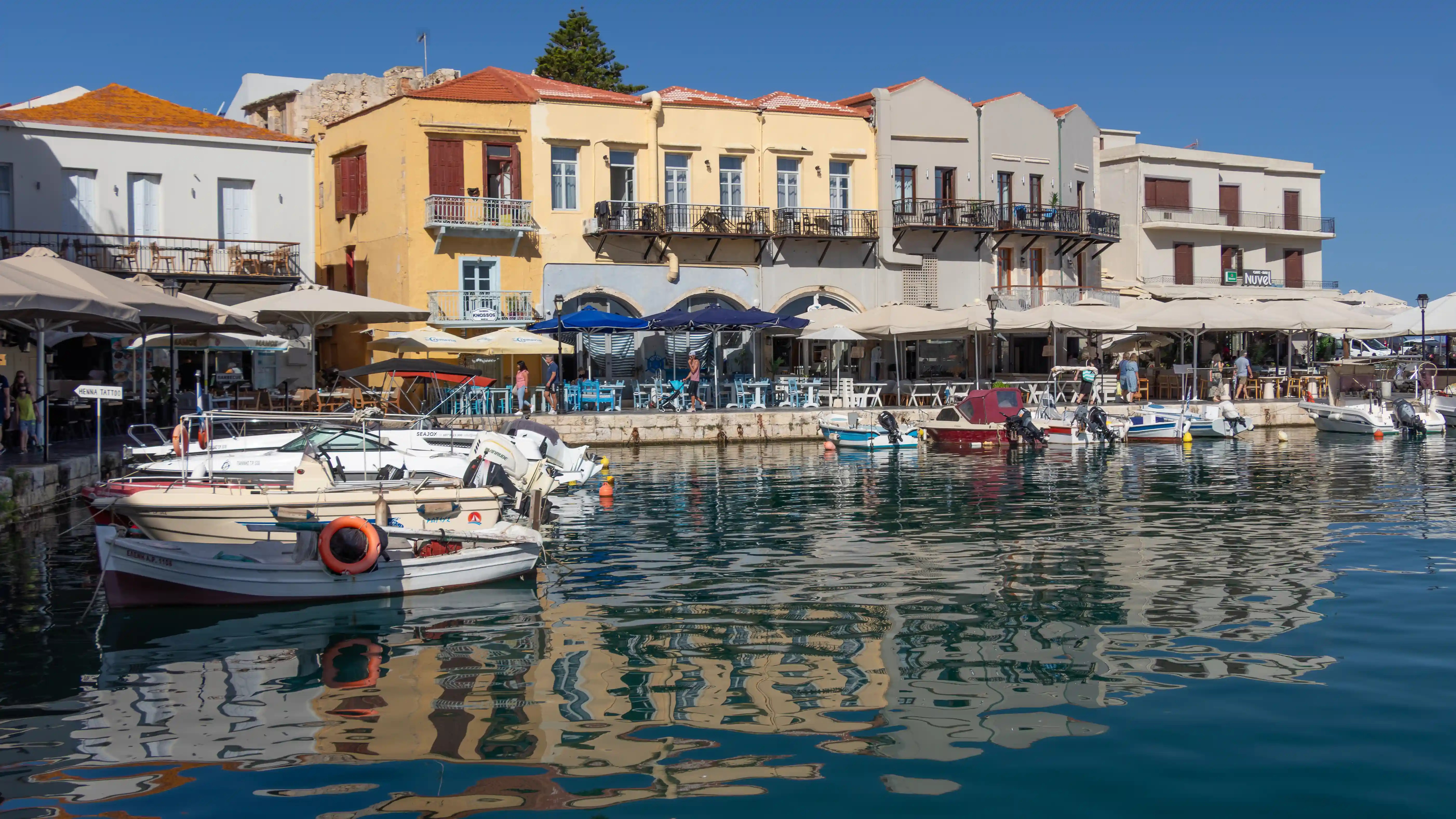 Boats tied along a waterfront lined with colorful buildings and outdoor cafés.