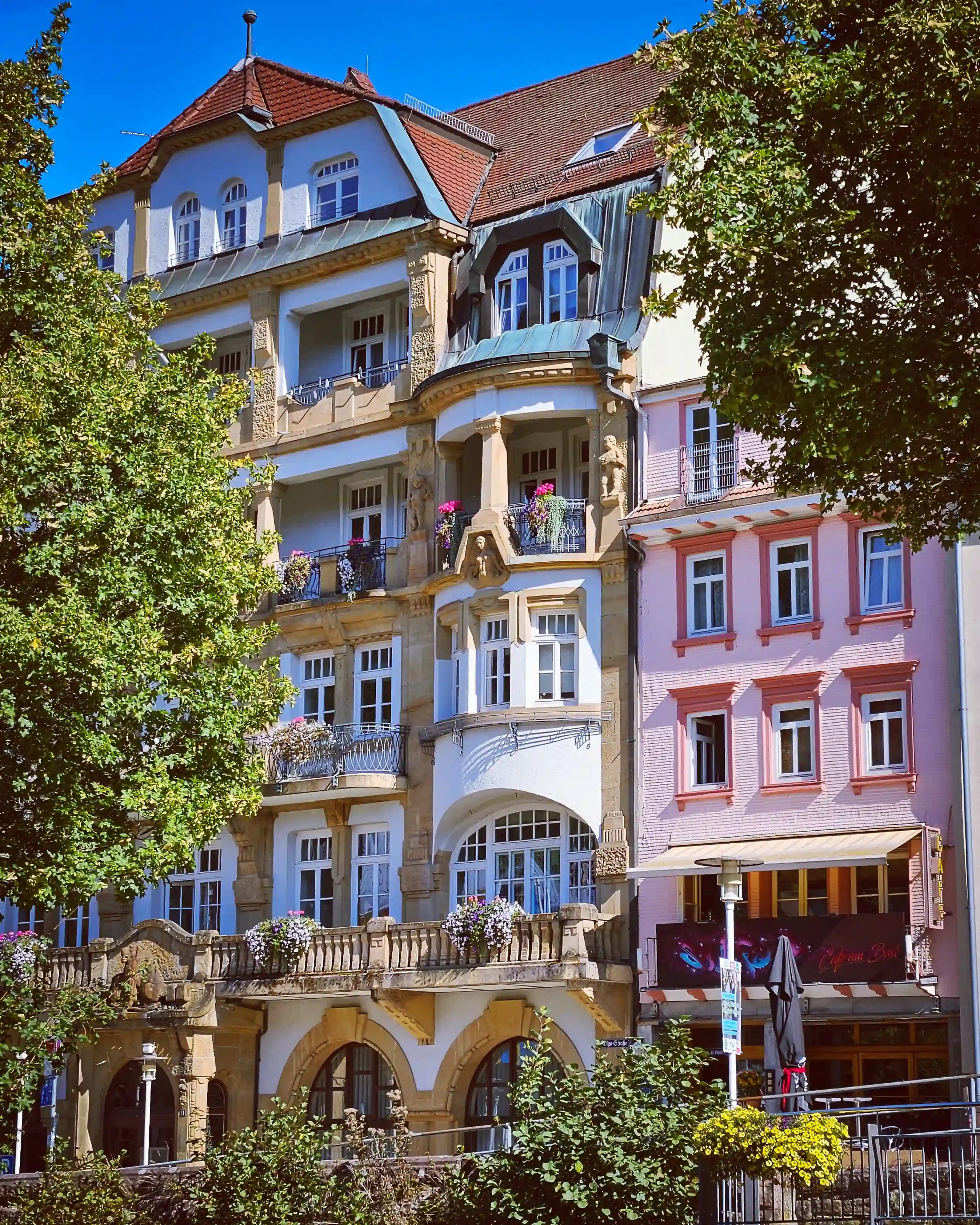 An ornate multi-story building with balconies and decorative details stands beside neighboring pastel buildings.