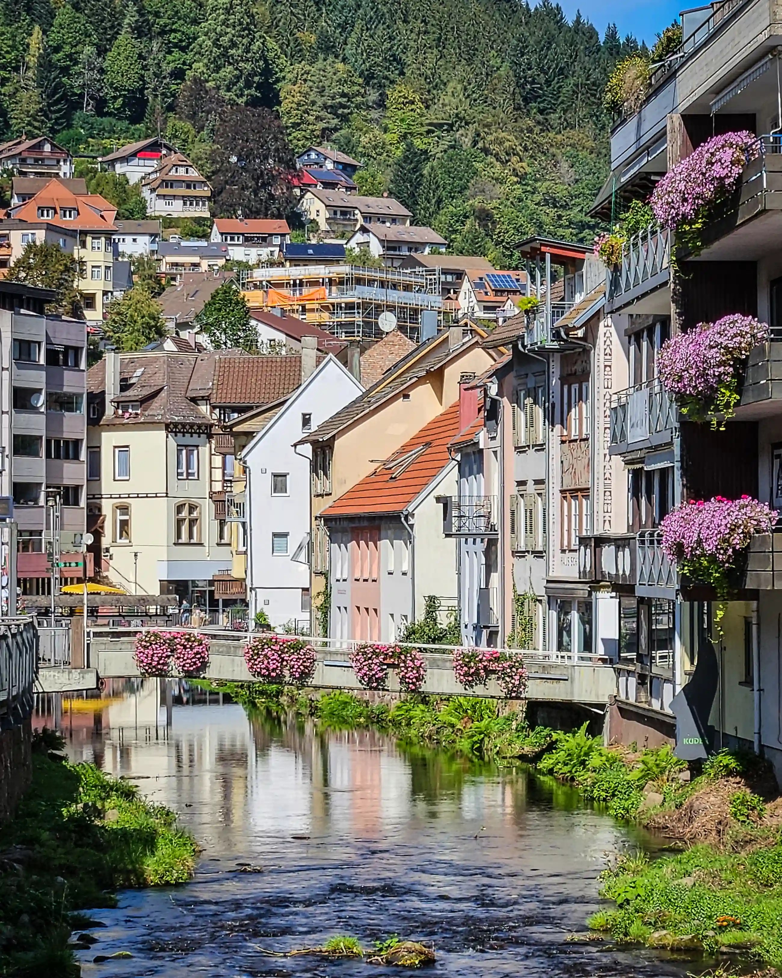 A river flows through a narrow town center with colorful buildings and balconies on both sides.