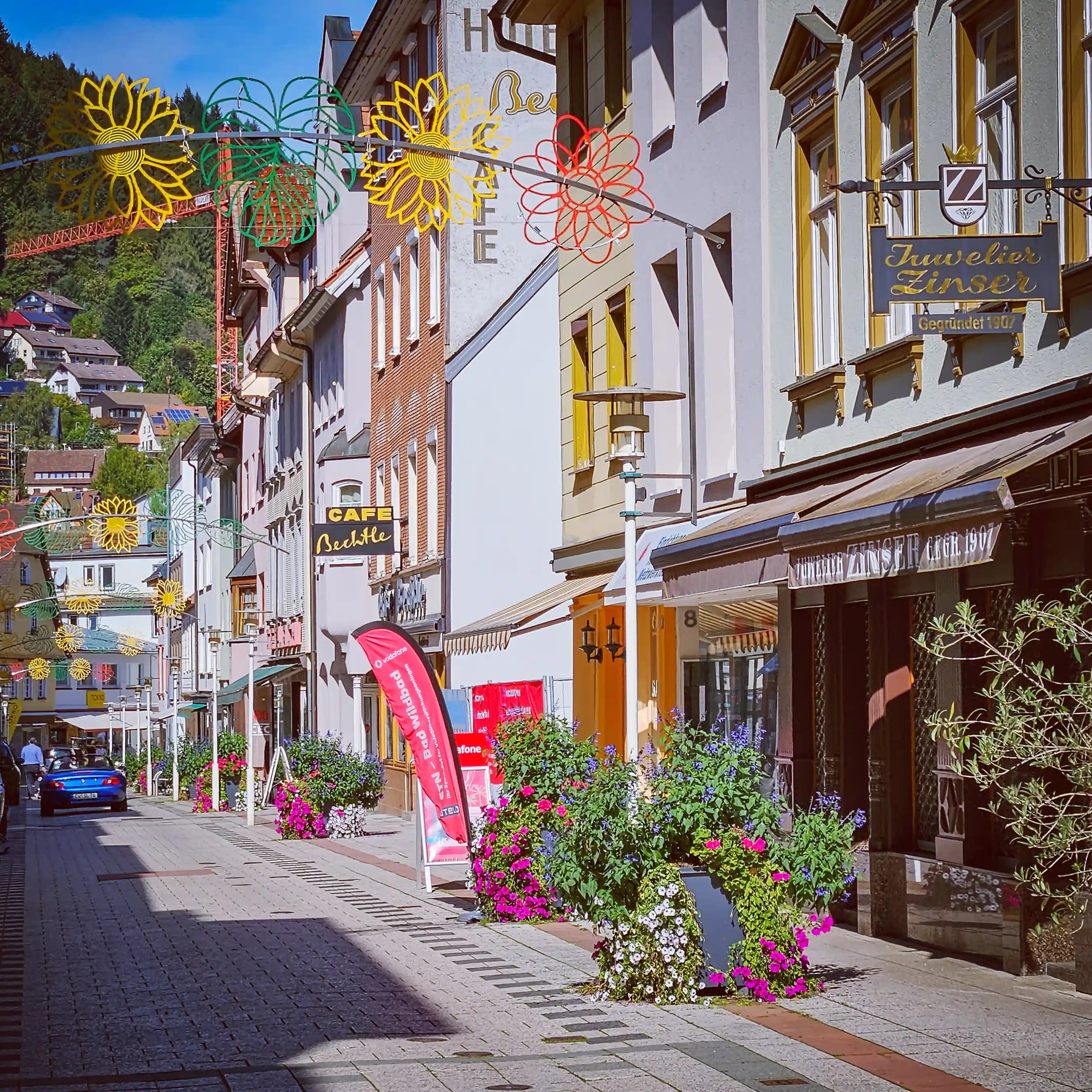 A pedestrian street lined with colorful buildings, flower planters, and hanging decorations in Bad Wildbad.