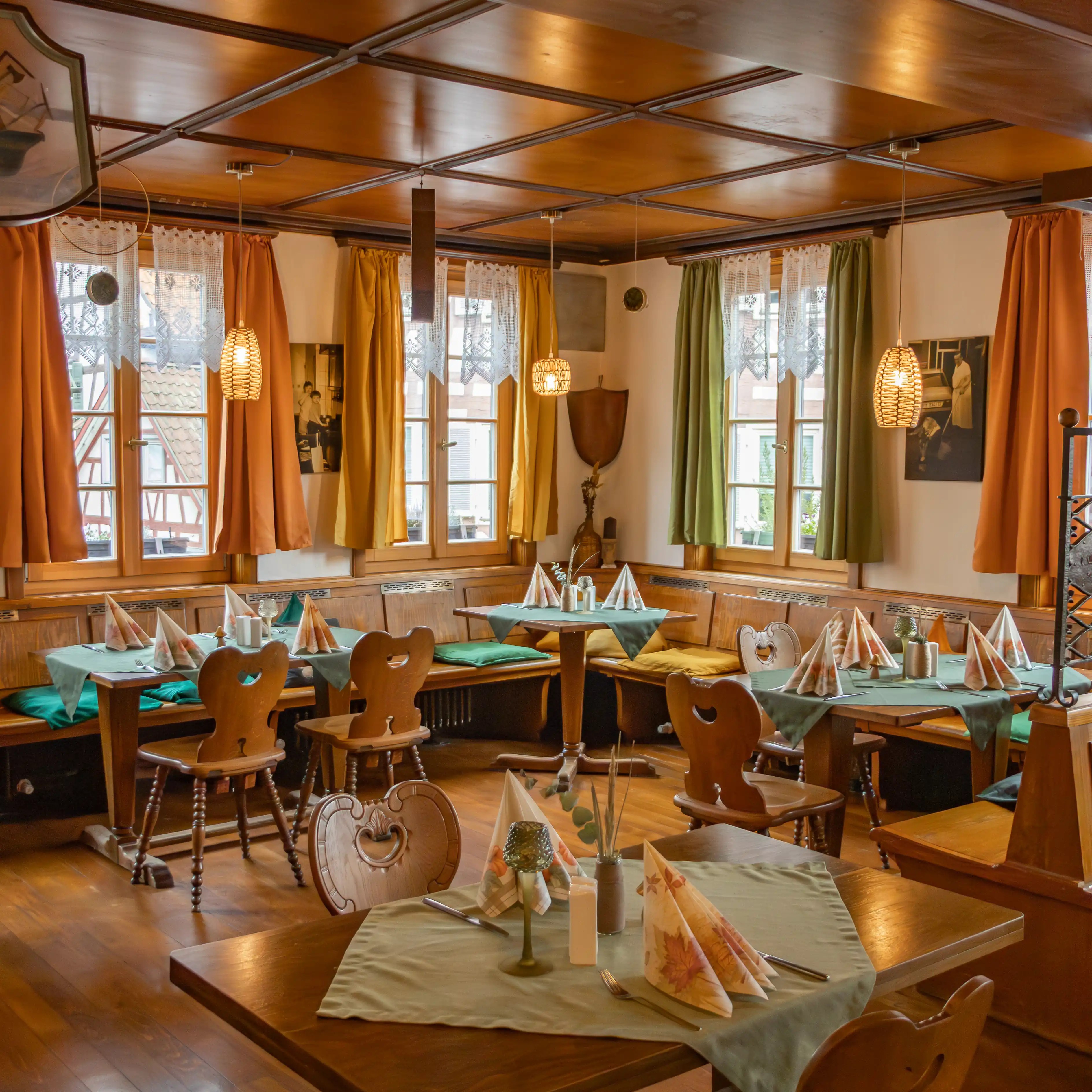 A warmly lit dining room with wooden tables, patterned curtains, and neatly set place settings inside a traditional restaurant in Calw.