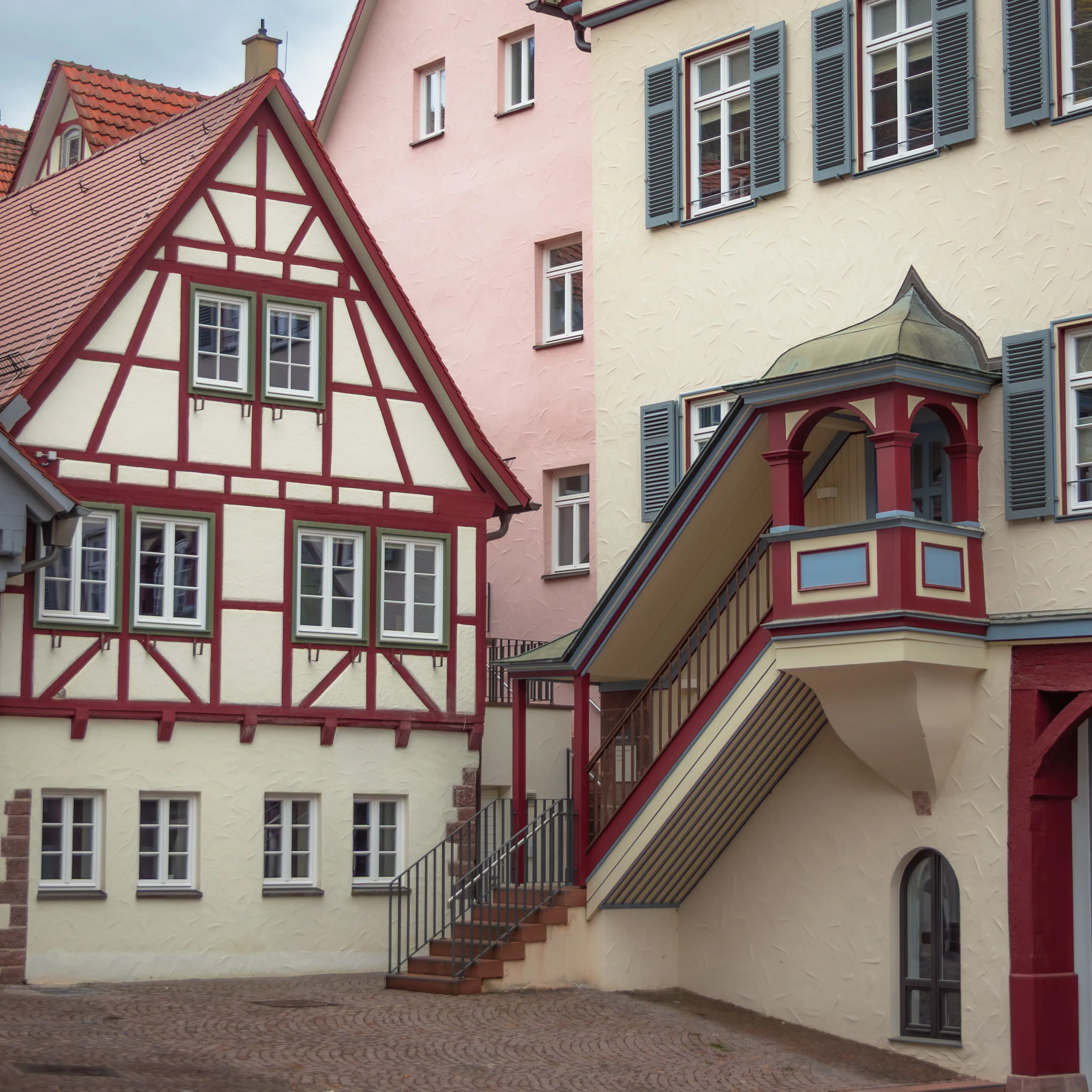 Two traditional houses in Calw, one half-timbered and one with shutters, one has an external staircase with red trim.