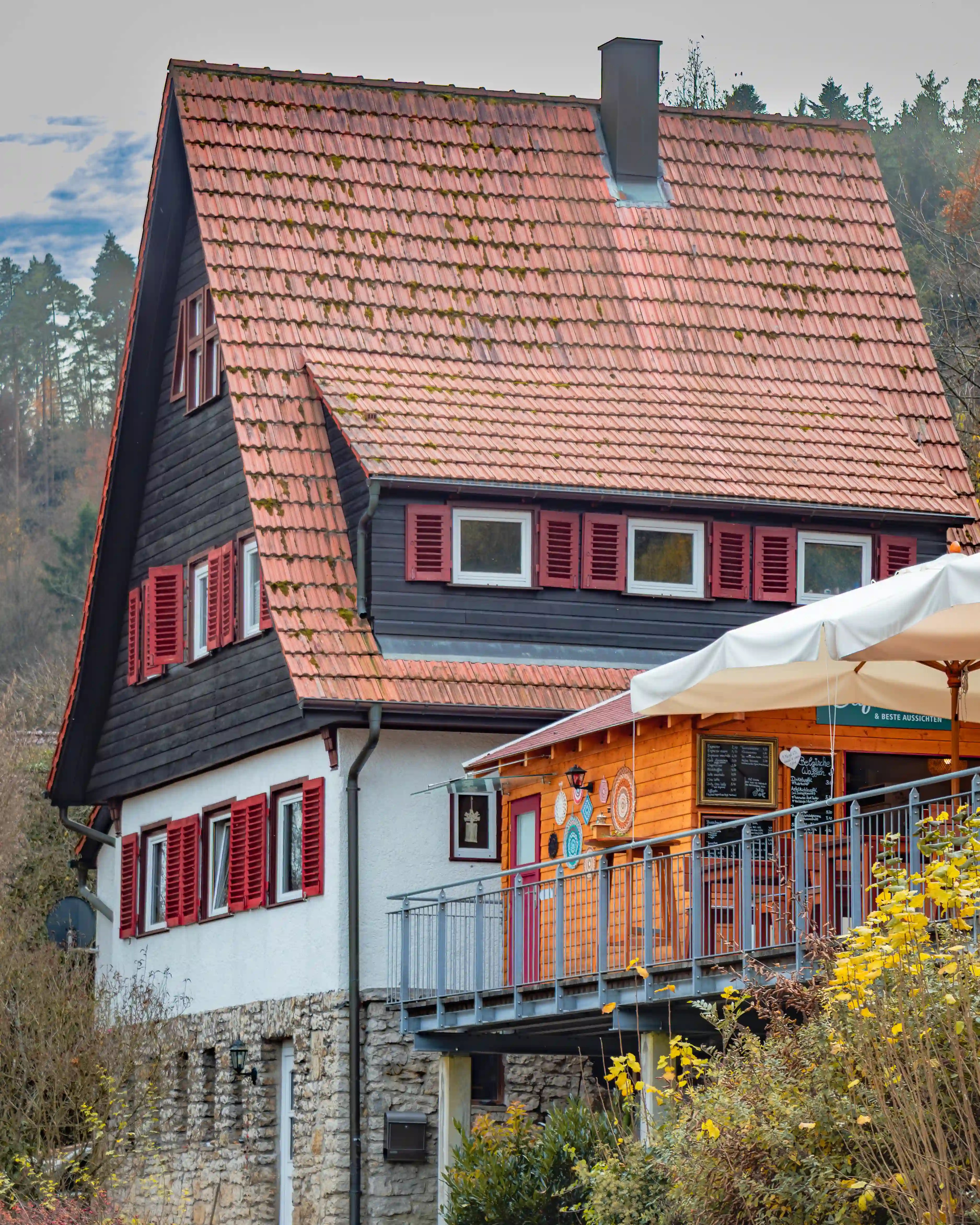 A house with red shutters and a steep tiled roof stands beside the terrace of Caféhäusle & Beste Aussichten.