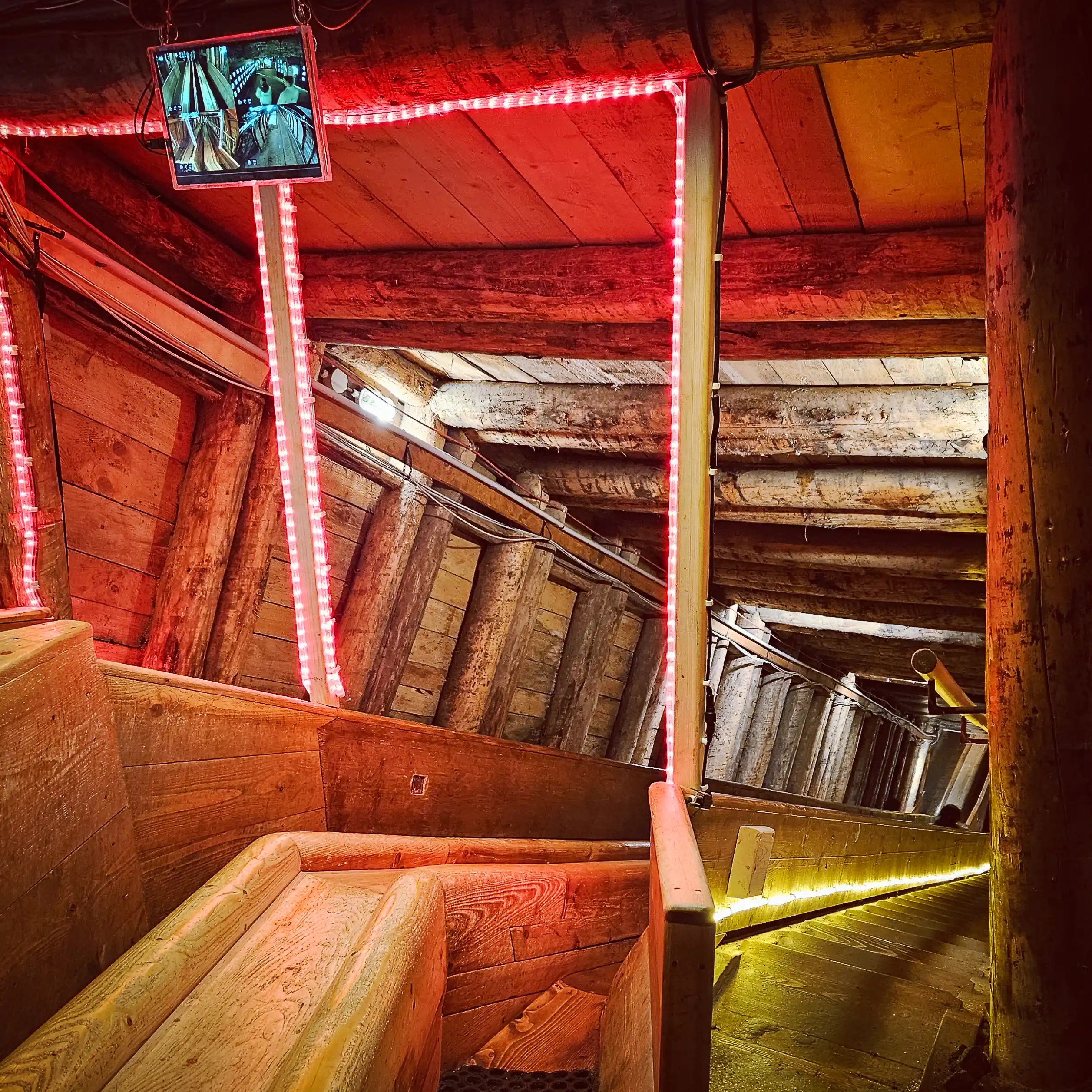 Interior of the salt mine showing a steep wooden slide, timber supports, a monitor displaying camera views, and LED strip lighting.