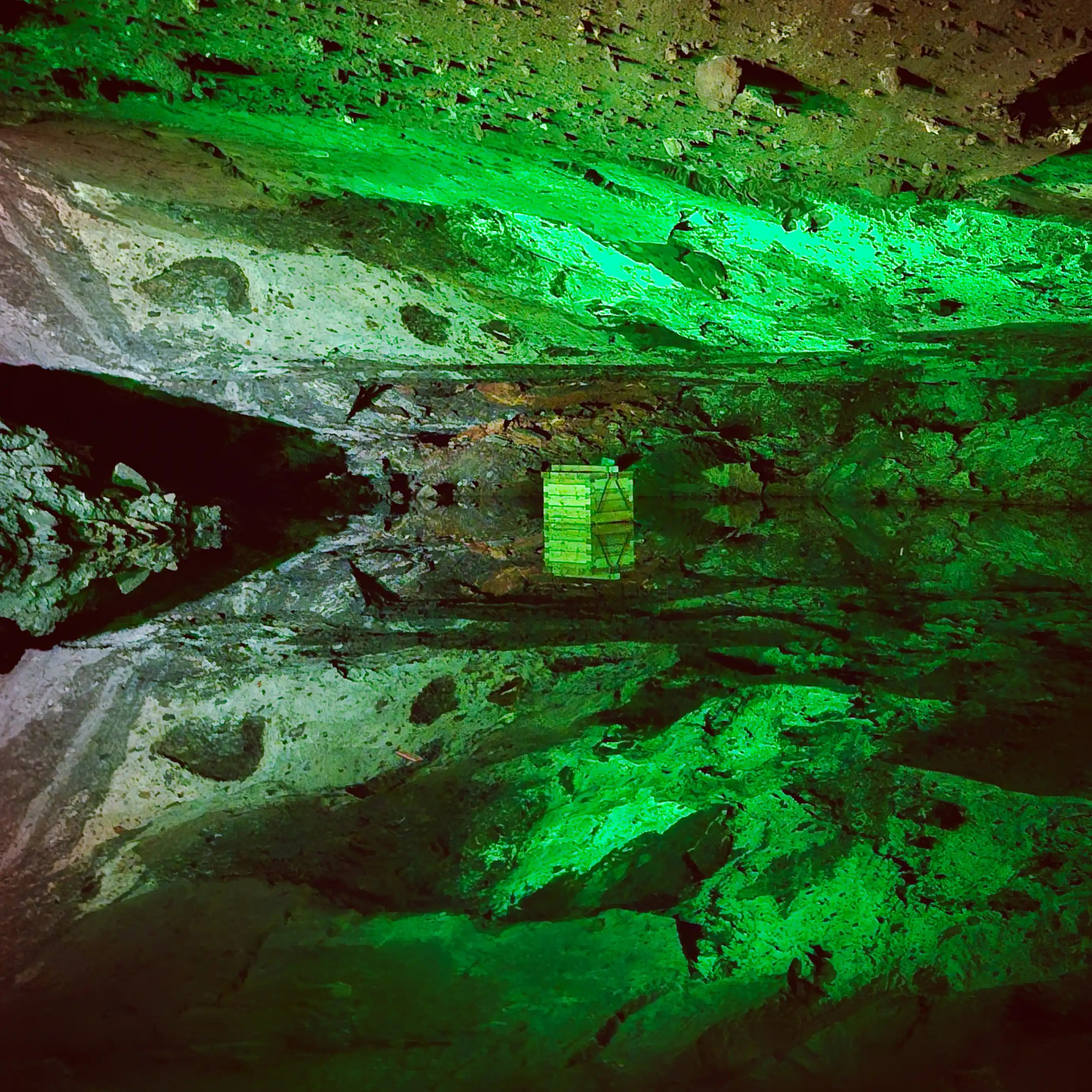 A still saltwater lake inside the Hallstatt Salt Mine reflecting green light, an illuminated box and the surrounding rock ceiling.