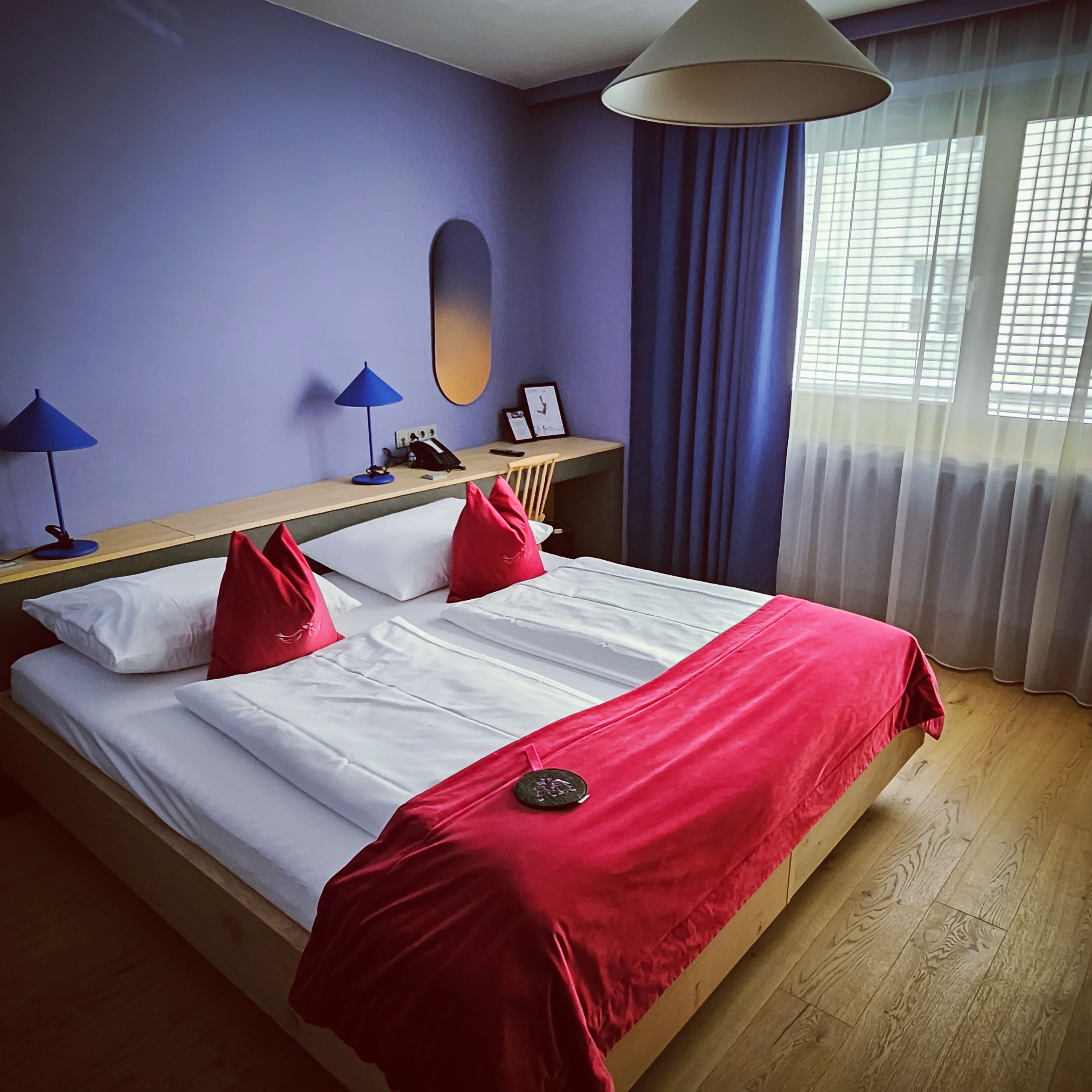 Modern hotel room at Hotel Weisse Taube in Salzburg with wooden floors, purple walls, and pink accent pillows.