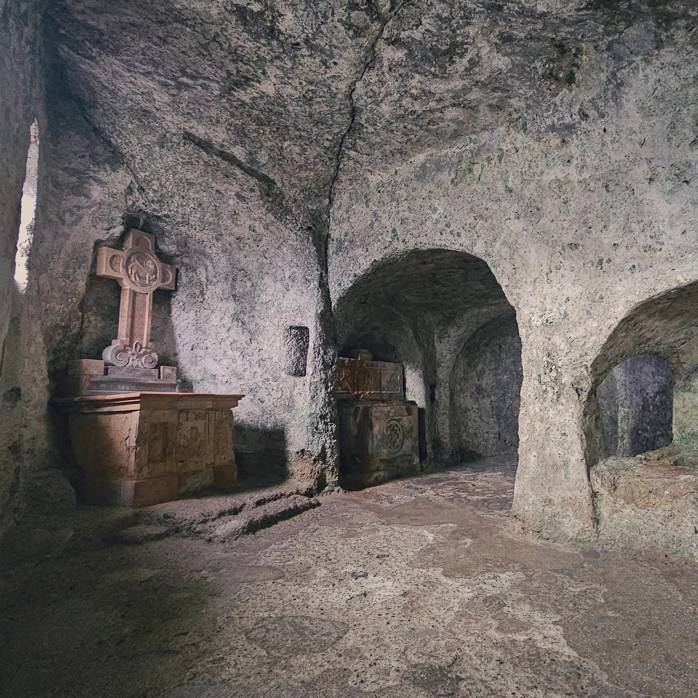 Rough stone archways and carved tombs line a dim rock-cut passage inside the St. Peter’s Catacombs.