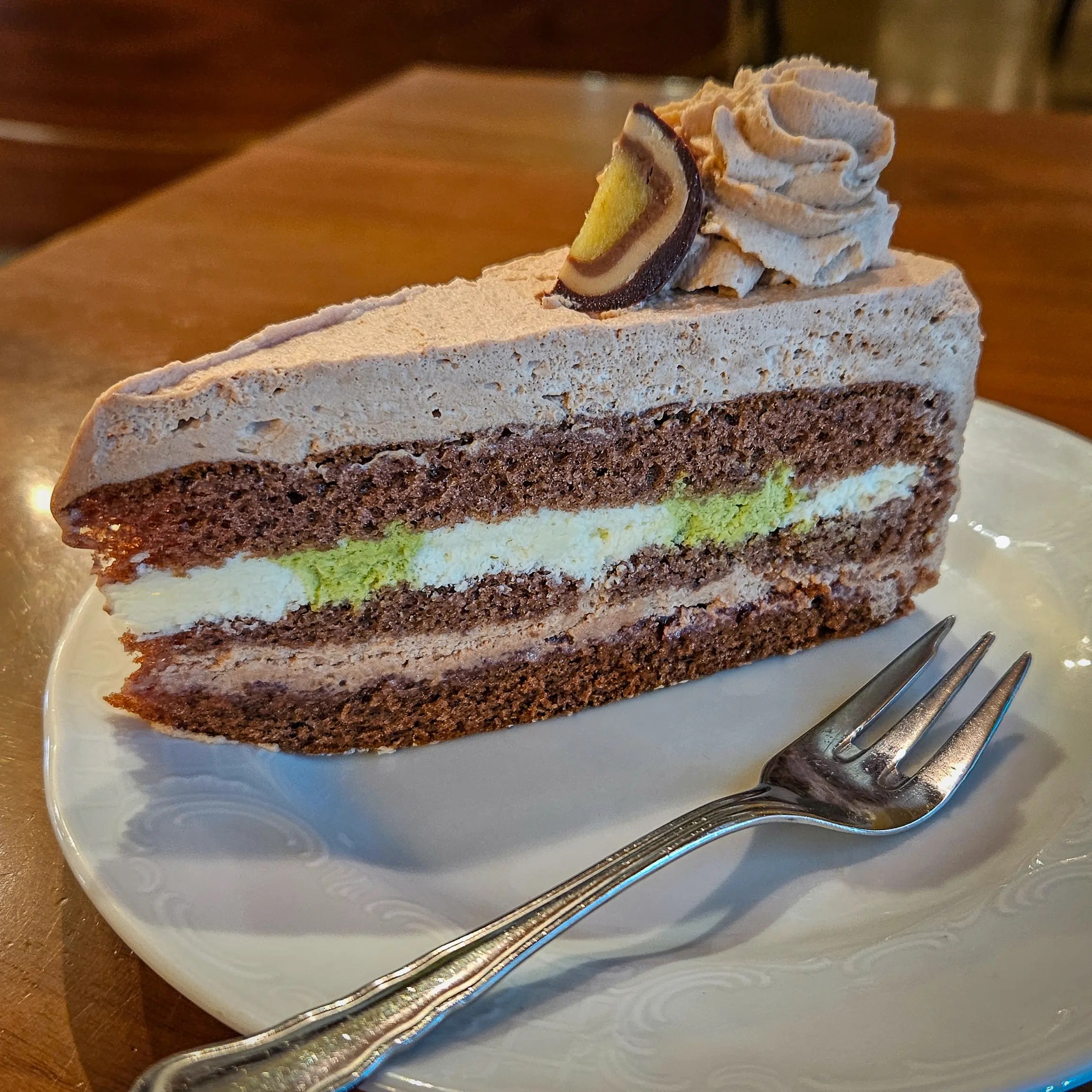 A slice of layered chocolate cake with light cream filling sits on a white plate with a fork at Café Mozart in Salzburg.