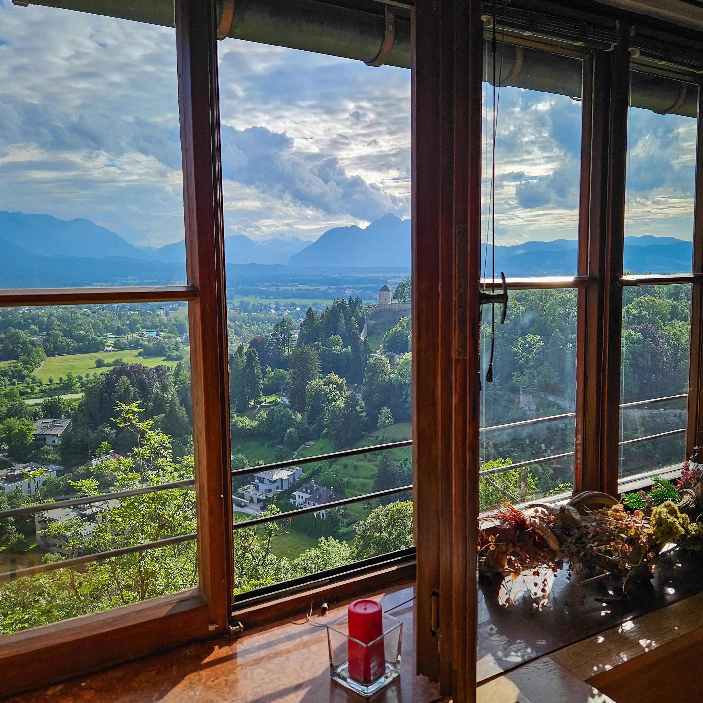 A wide landscape view of green hills, trees, and distant mountains seen through tall wooden-framed windows from inside the fortress.