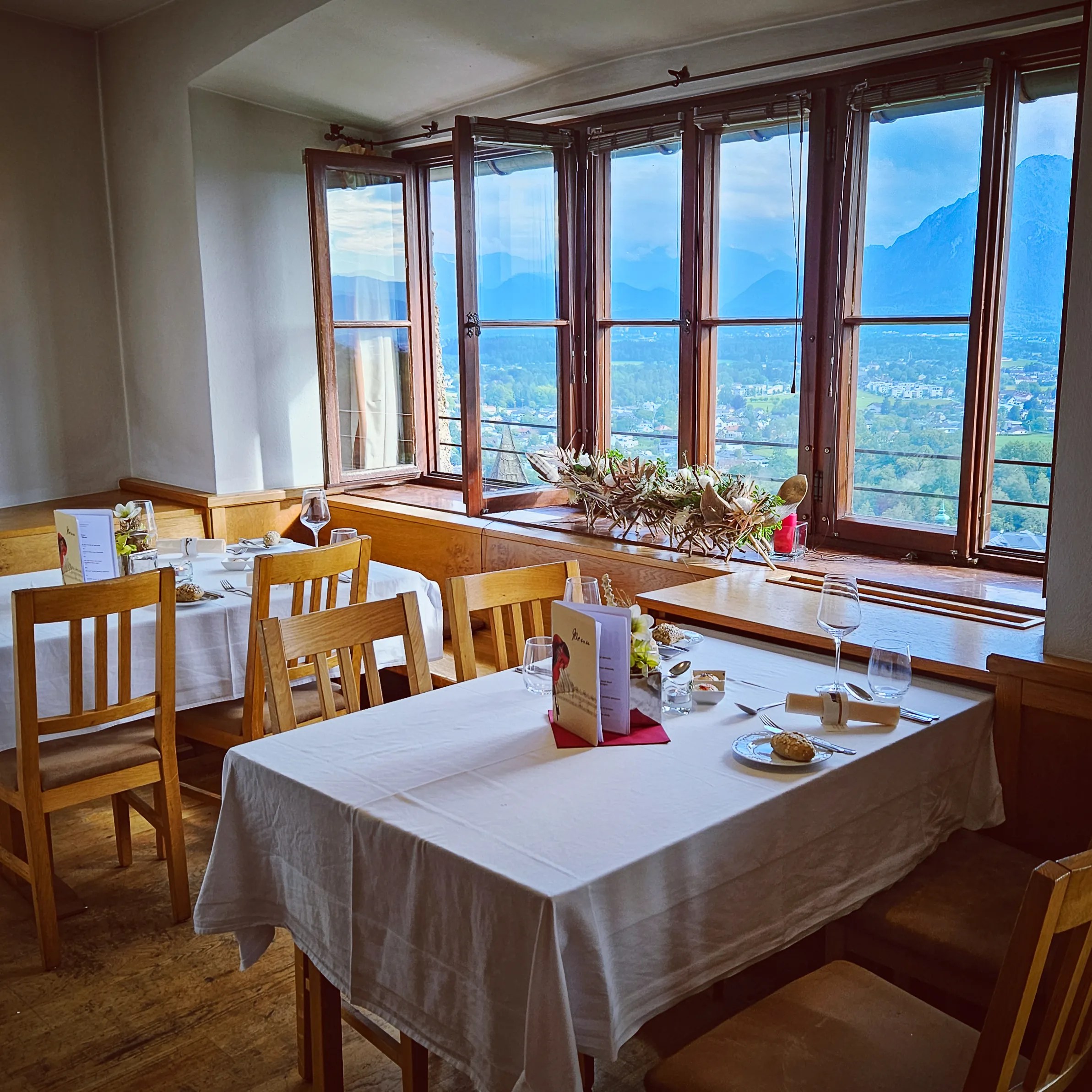 A dining room with white tablecloths and wooden chairs set beside large windows overlooking the Salzburg landscape.