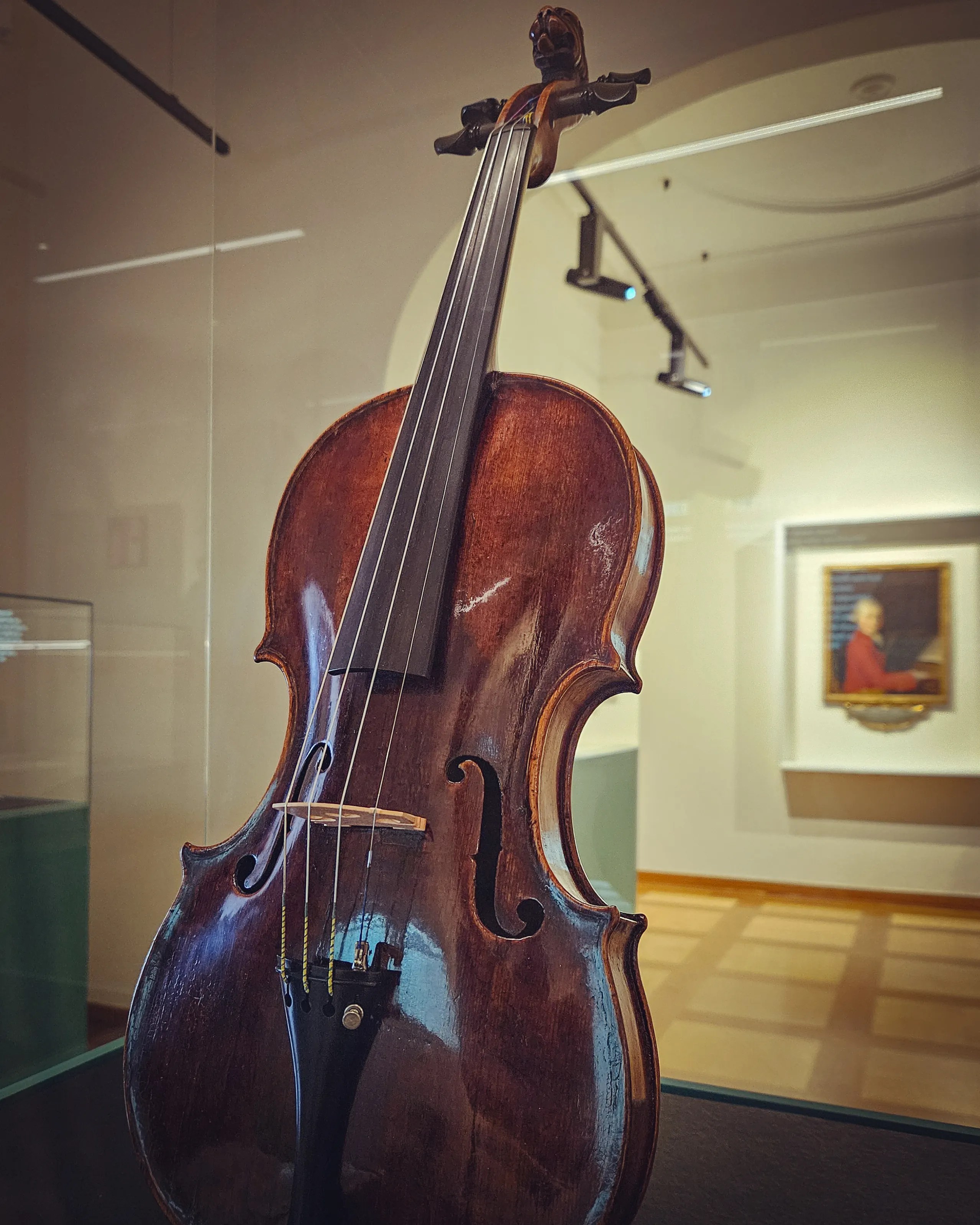 Mozart’s original violin displayed upright in a glass case inside Mozarts Geburtshaus, with a softly lit museum gallery in the background.