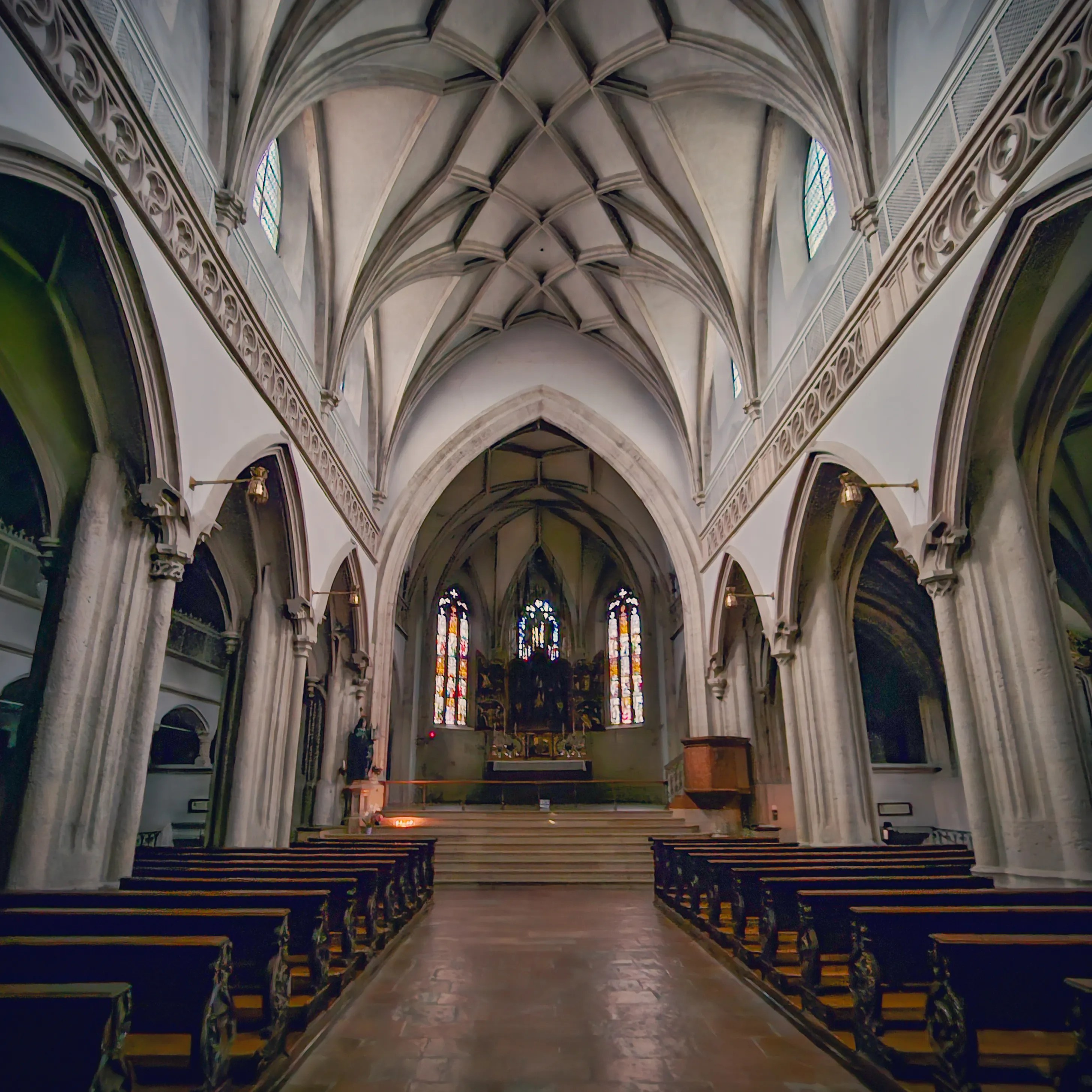 The Gothic interior of Salzburg Nonnberg Abbey church with tall stone columns, ribbed vaulted ceilings, wooden pews, and the ornate high altar at the far end.