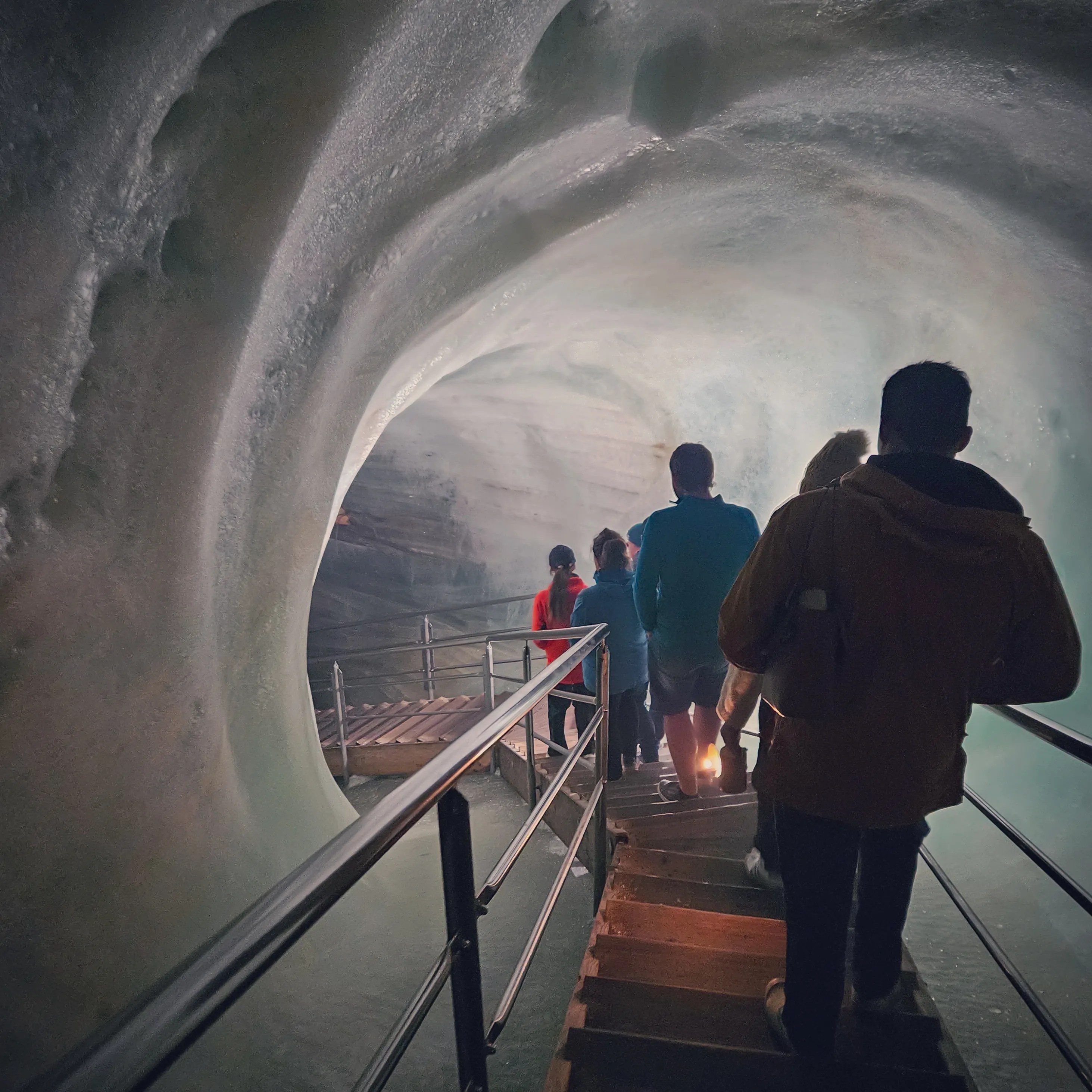 Visitors descend a staircase carved through ice inside Eisriesenwelt, surrounded by curved frozen walls and metal railings.