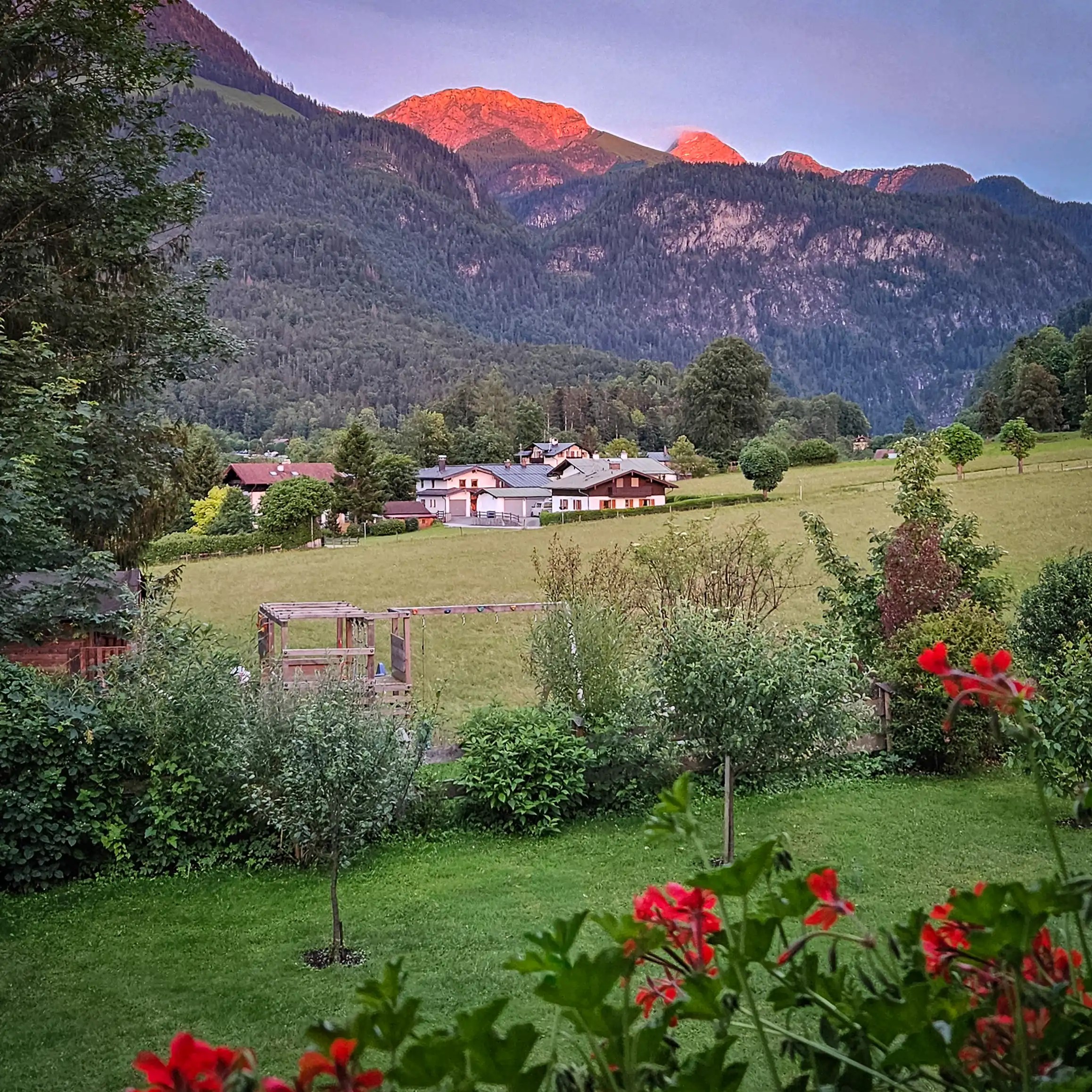 Mountain peaks glowing orange from the setting sun above a quiet Alpine village.