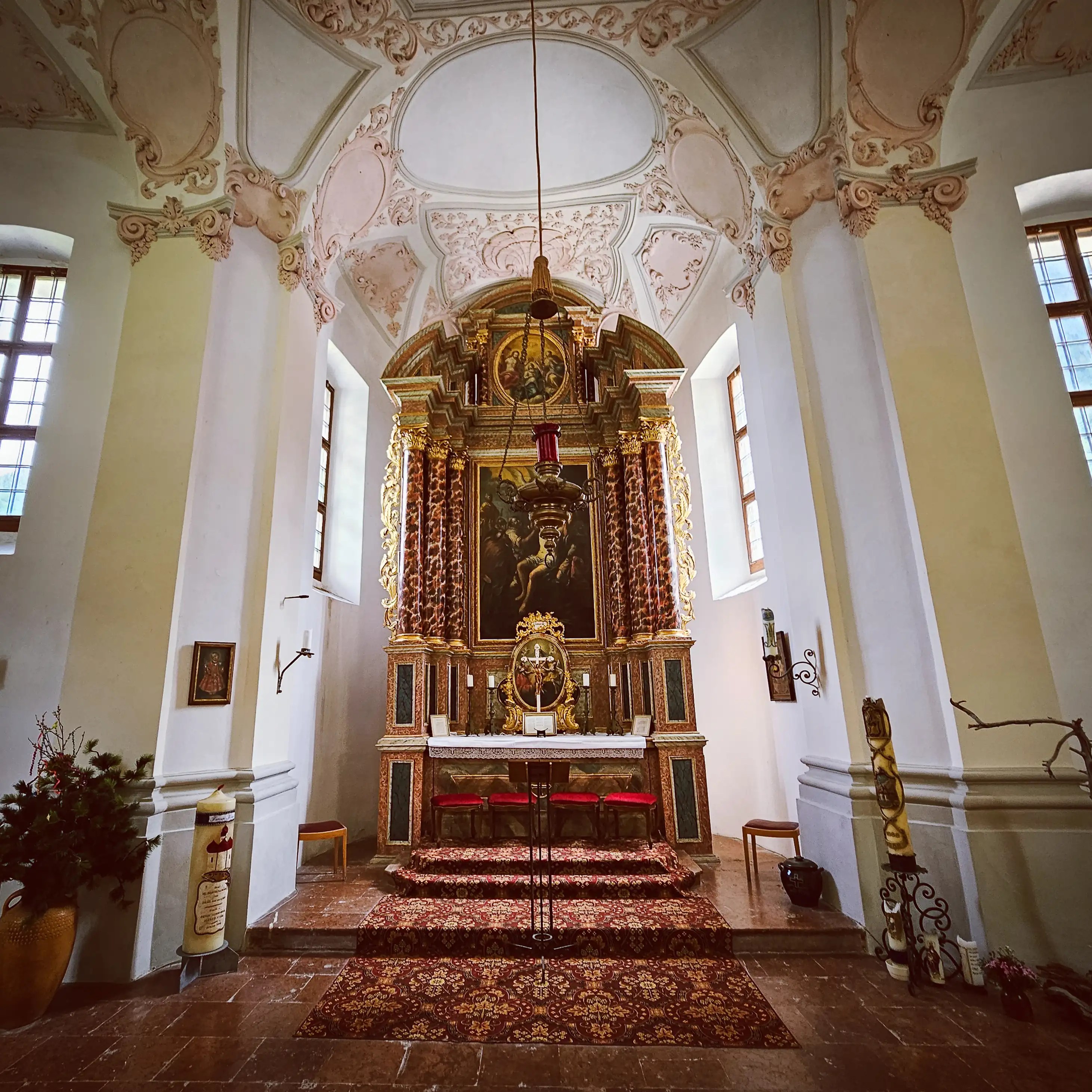 The richly decorated main altar of the Church of St. Bartholomä stands beneath a pale pink and white stucco ceiling.
