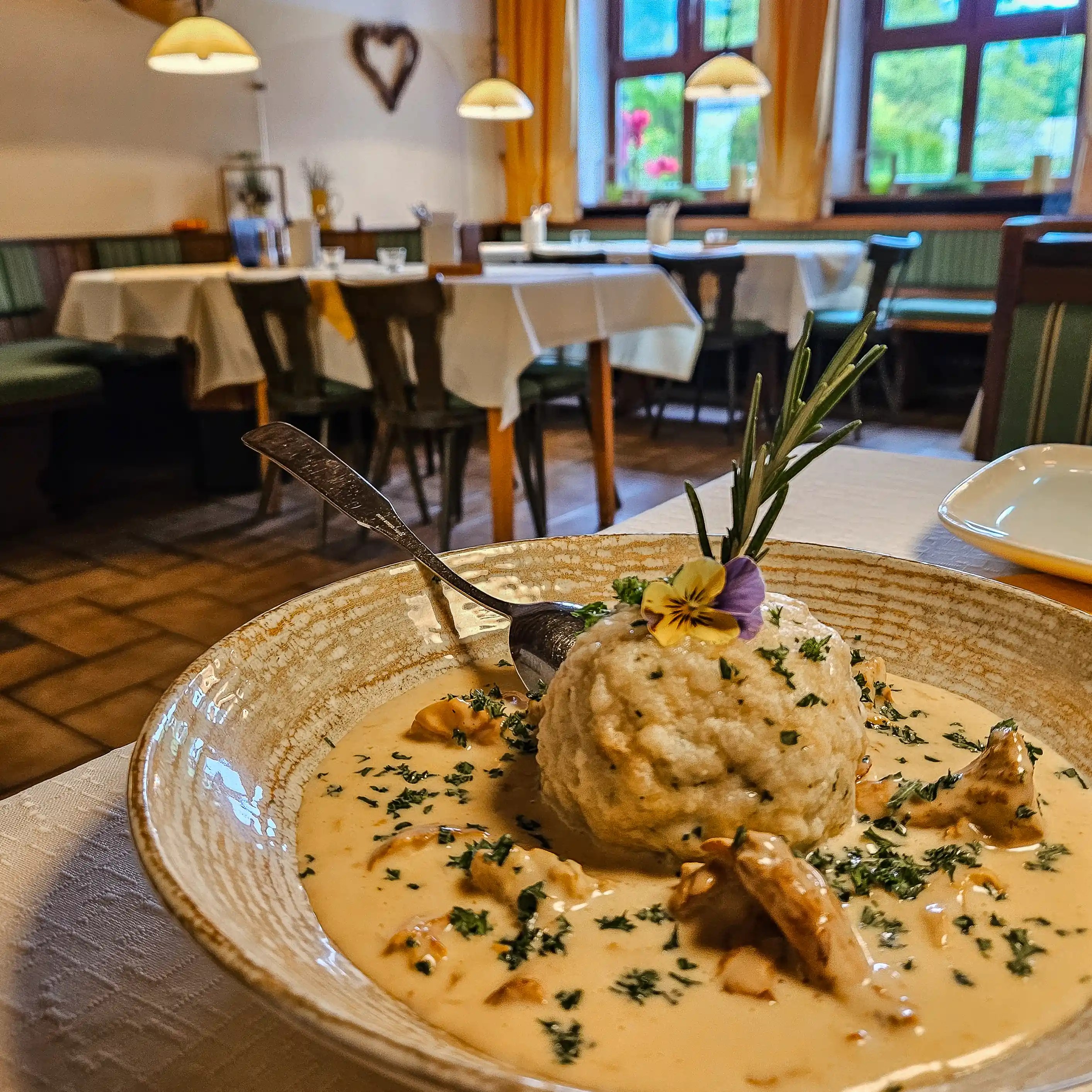 A plate of bread dumpling topped with herbs and an edible flower, served in a creamy mushroom sauce.